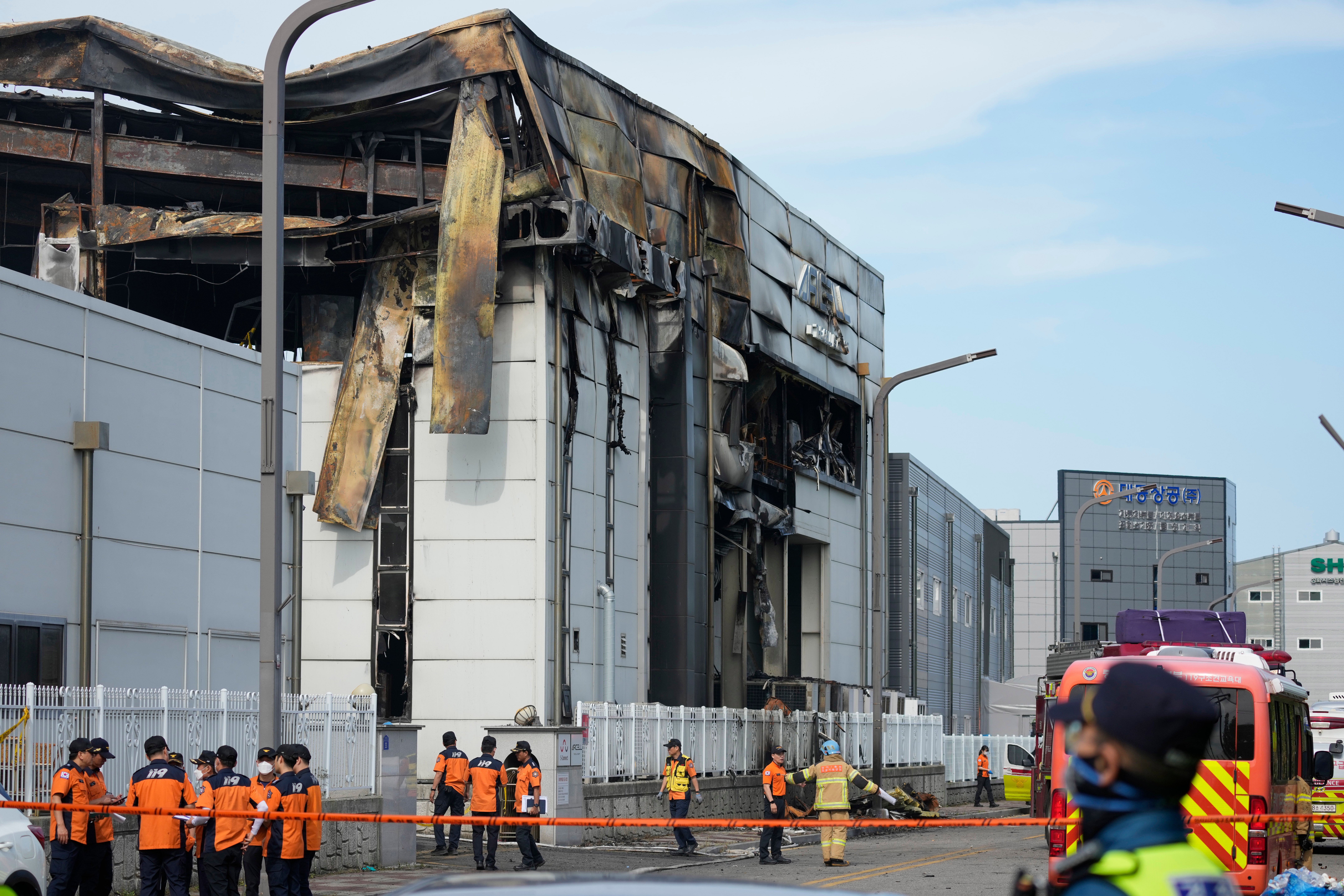 Firefighters and a police officer work outside of the site of a burnt battery manufacturing factory in Hwaseong, South Korea