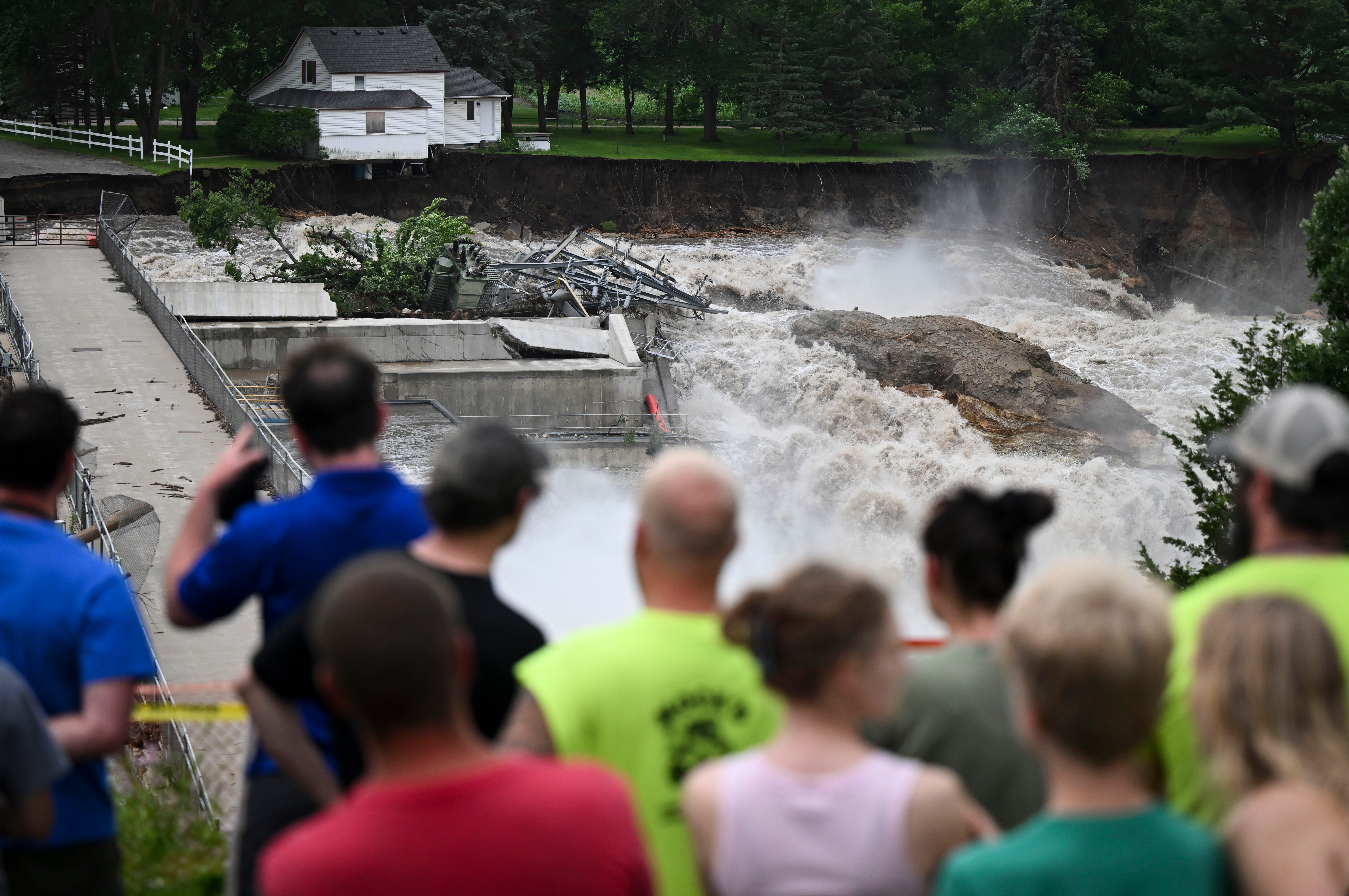 A crowd watches a home on the brink of collapse near the Rapidan Dam in Minnesota. Severe flooding and debris caused the dam to partially fail on Monday