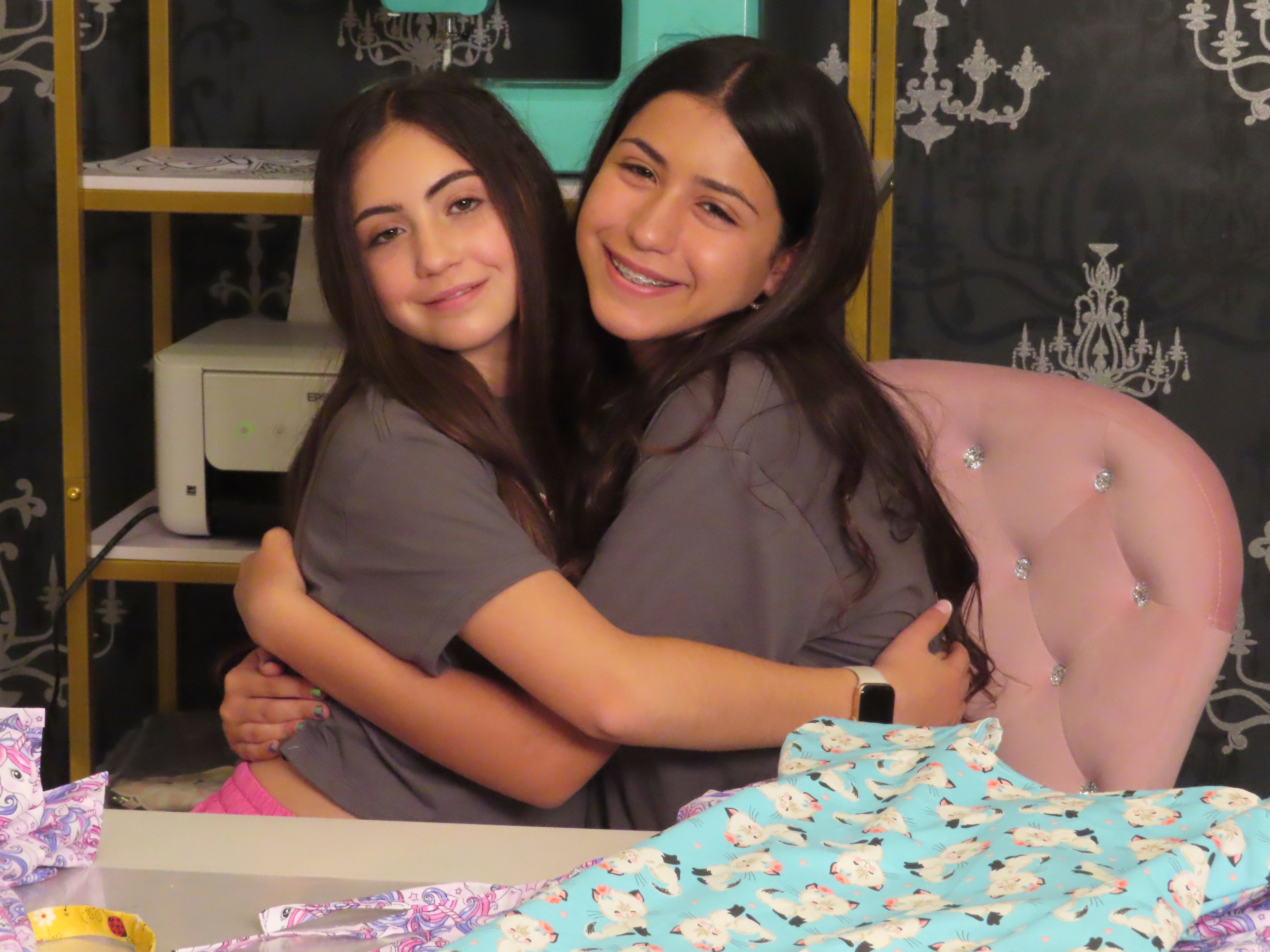 Audrina Demma, left, and her sister Giuliana hug in the basement at the sewing station of their Freehold, New Jersey, home on June 19, 2024. The sisters have sewn and donated 1,800 hospital gowns to sick children in 36 states plus Africa. Giuliana was inspired by seeing her baby cousin wearing an ugly, ill-fitting gown while hospitalized with brain cancer in 2017