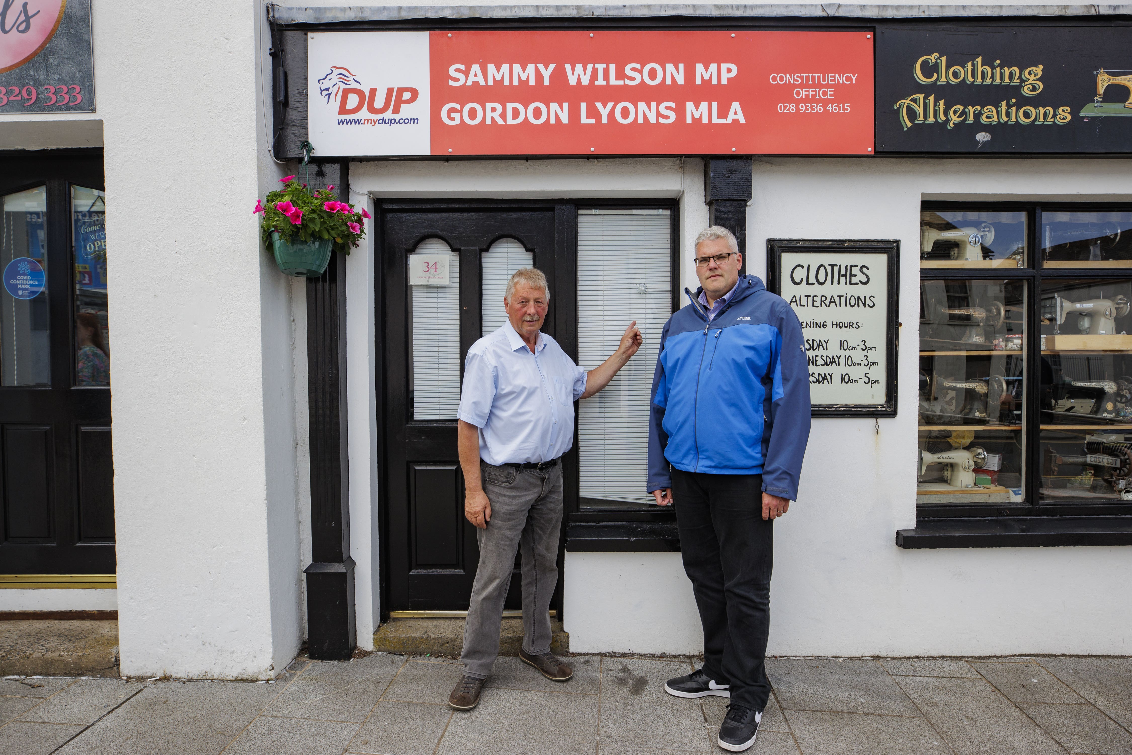 The DUP’s Sammy Wilson (left) and party leader Gavin Robinson stand beside the damage from four projectiles to the window and door of the offices of DUP parliamentary candidate Mr Wilson (Liam McBurney/PA)