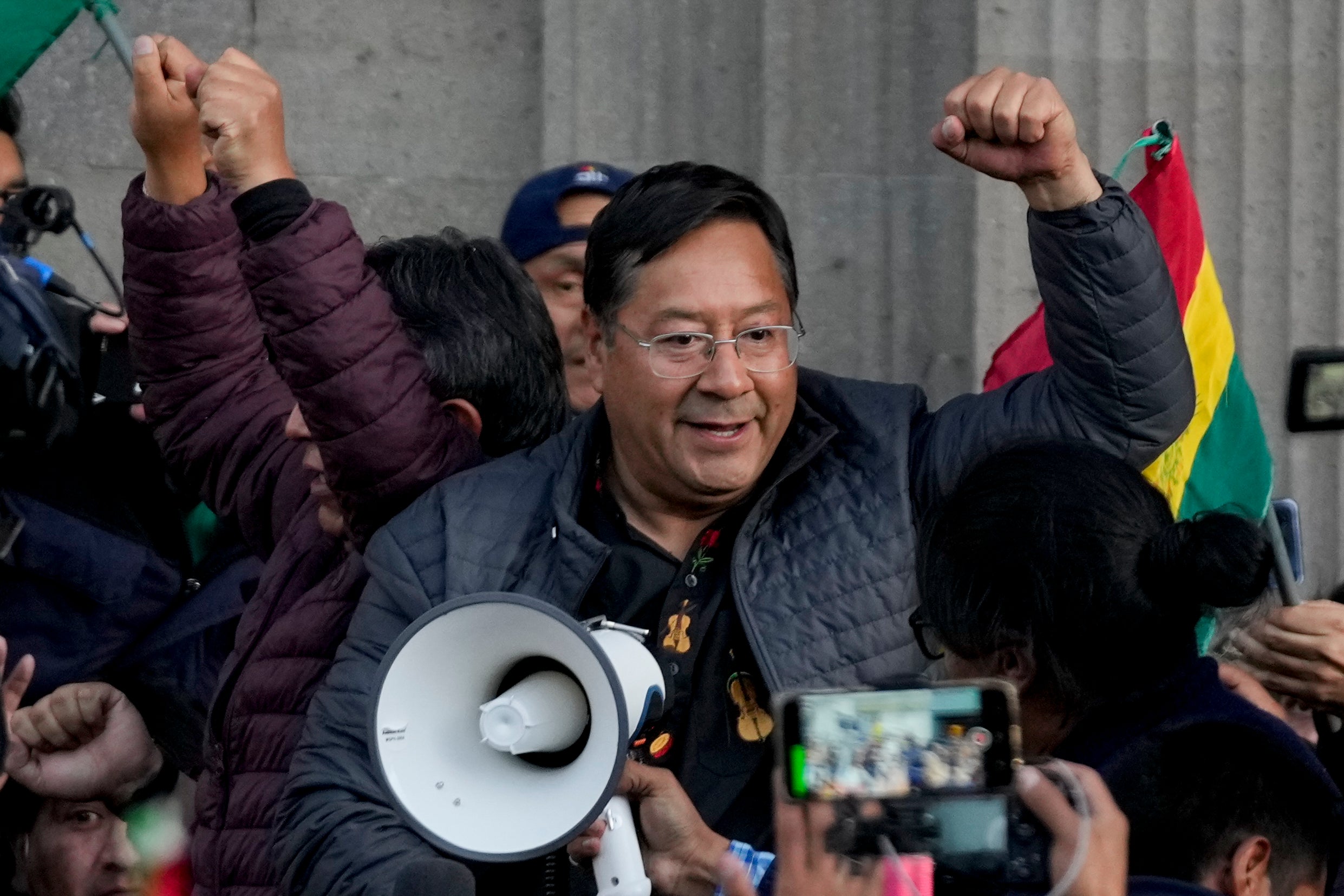 Bolivian President Luis Arce raises a clenched fist surrounded by supporters and media, outside the government palace in La Paz, Bolivia, Wednesday, June 26, 2024