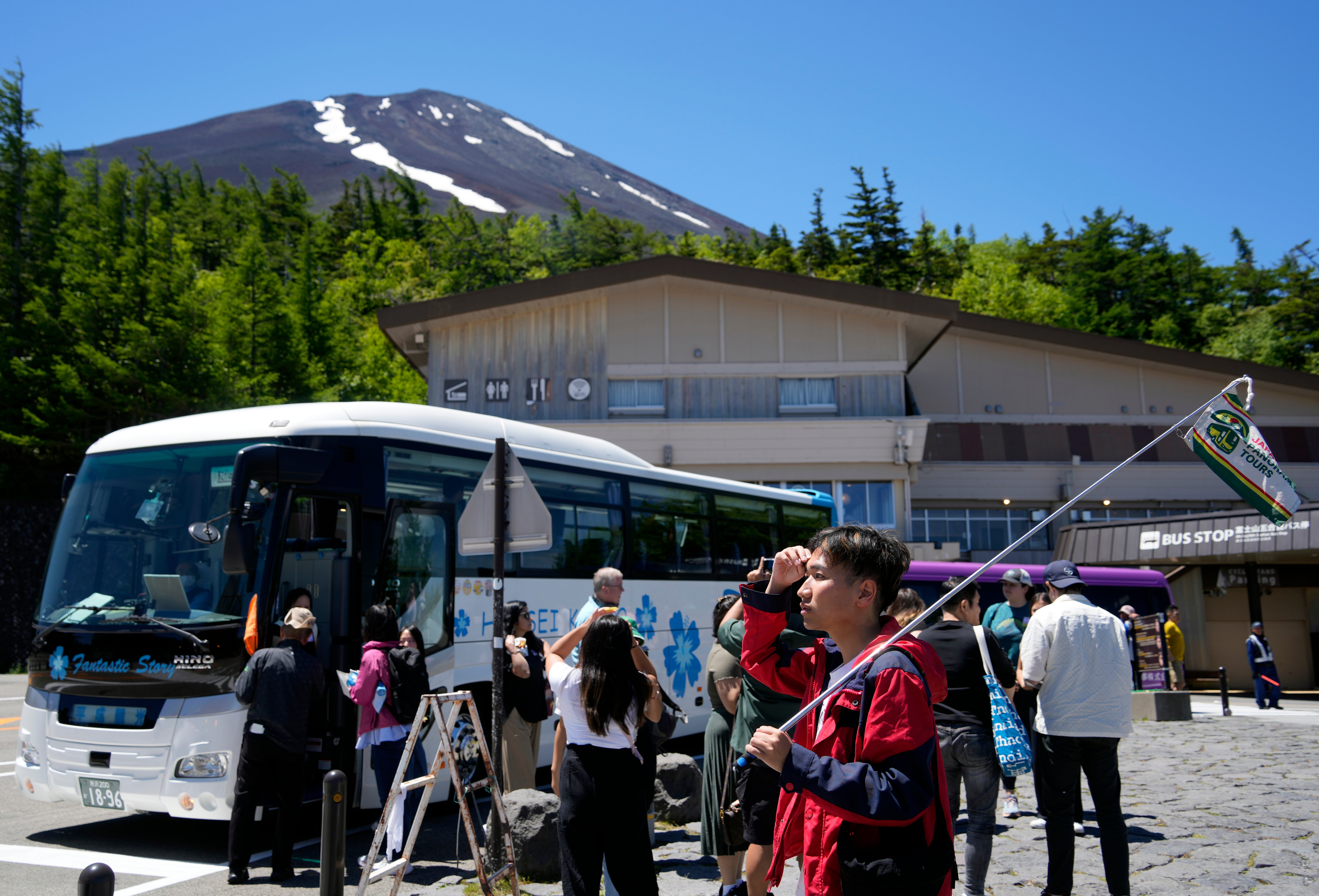 A tour conductor holds a flag at Mount Fuji 5th station as the summit is seen in the background in Yamanashi prefecture, Japan, on 19 June 2024