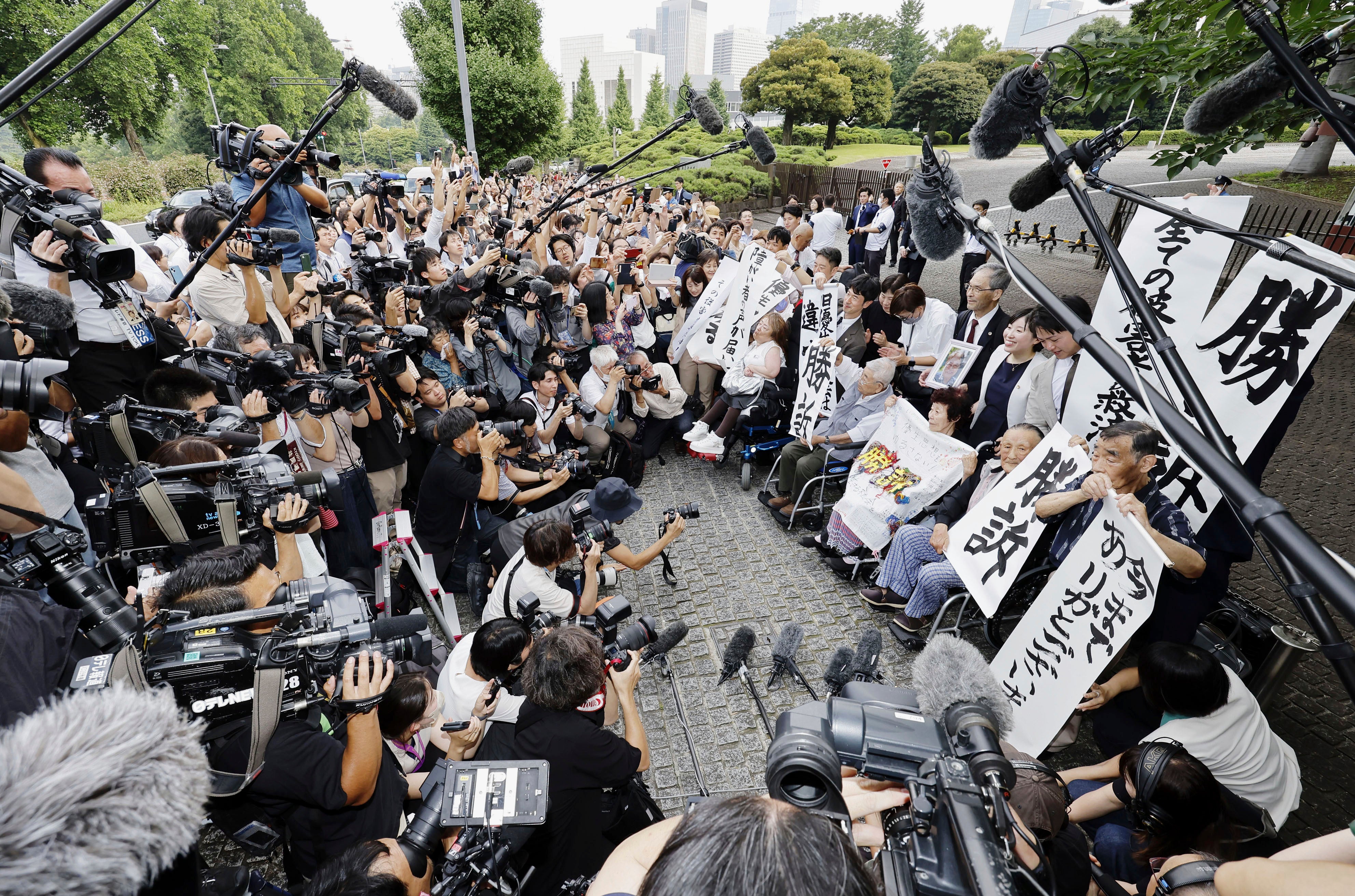 The plaintiffs, their lawyers and supporters hold the signs reading ‘Winning lawsuit’ outside the Supreme Court after in Tokyo, Japan, Wednesday, 3 July 2024