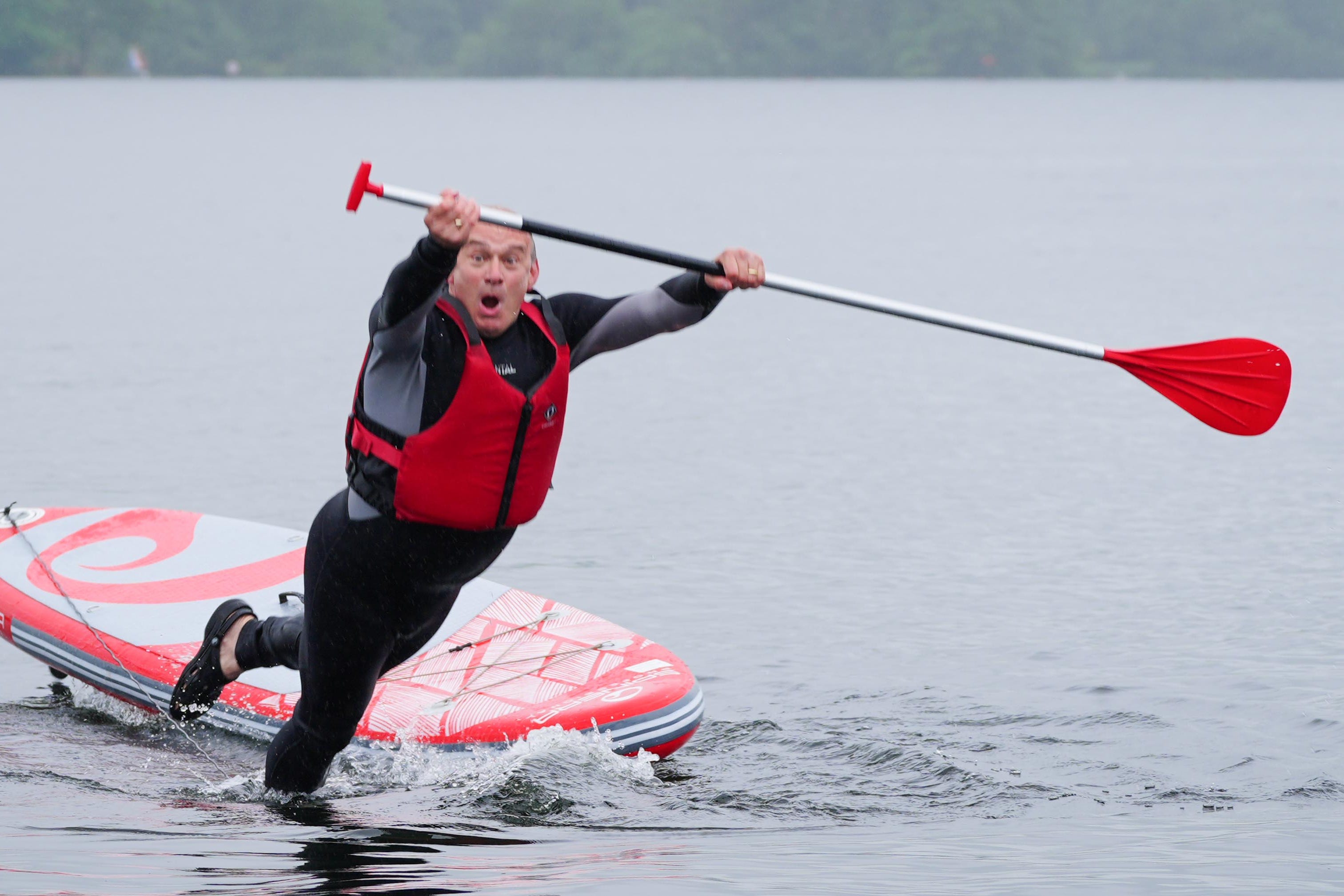 Liberal Democrat leader Sir Ed Davey topples off a paddleboard into Windermere, in the Lake District, one of several stunts he took part in on the campaign trail (Peter Byrne/PA)