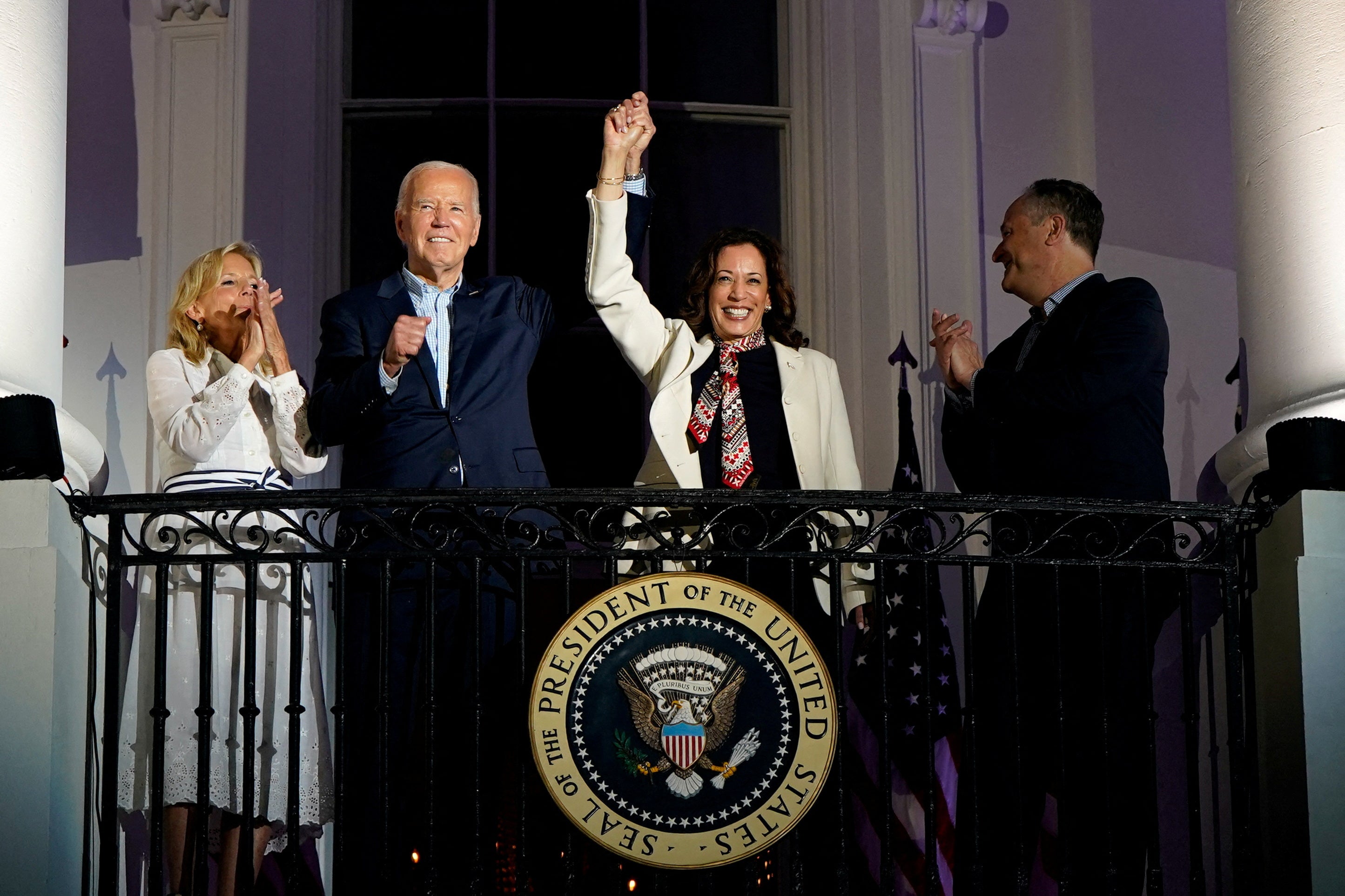 Biden andHarris raise their hands as they stand on a White House balcony on July 4th