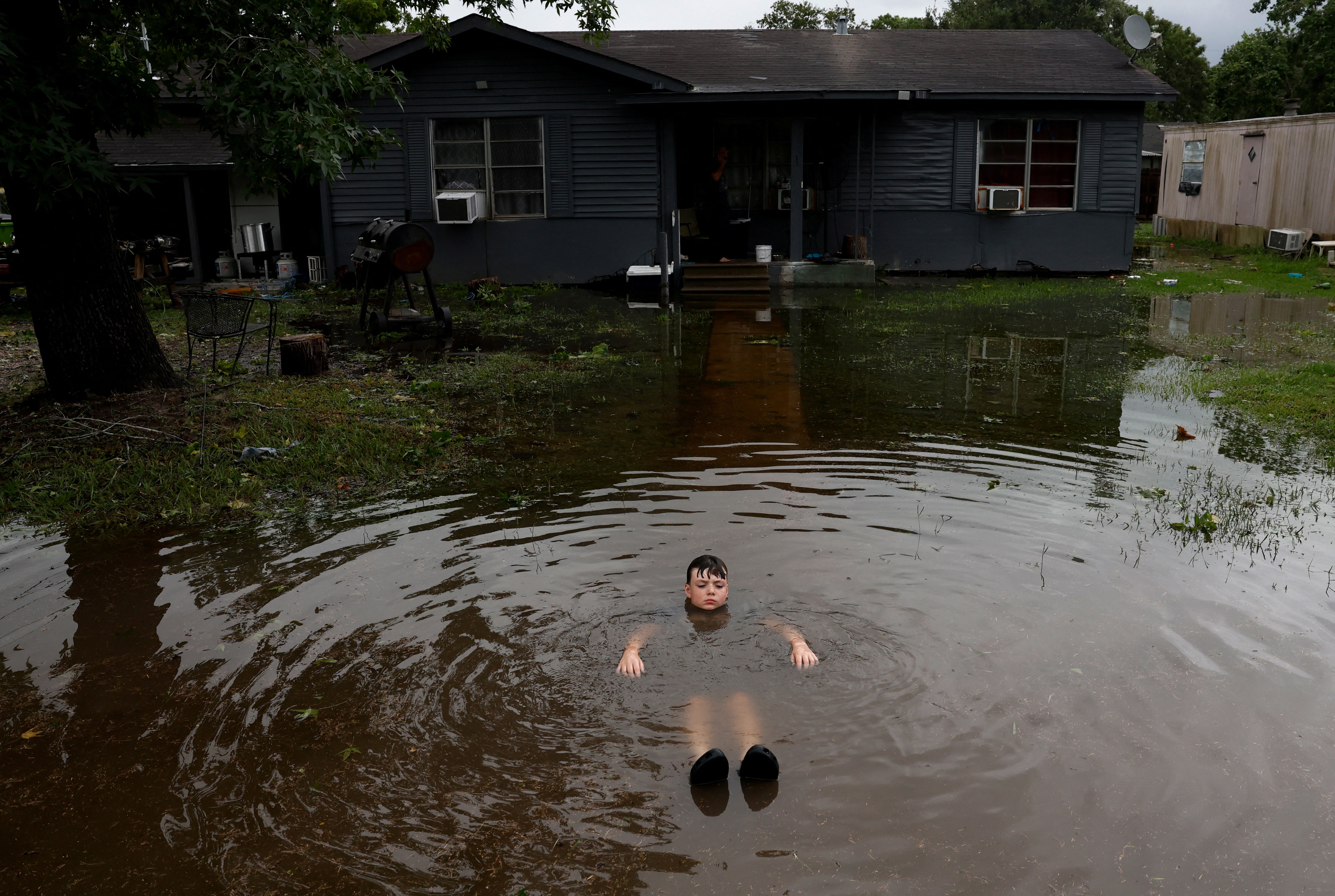 A boy immerses himself in flood waters outside a home in the aftermath of Beryl, in Rosenberg, Texas