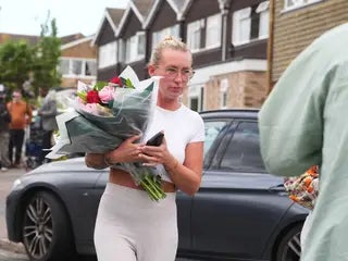 A woman delivers floral tributes near to the scene in Ashlyn Close, Bushey, Hertfordshire