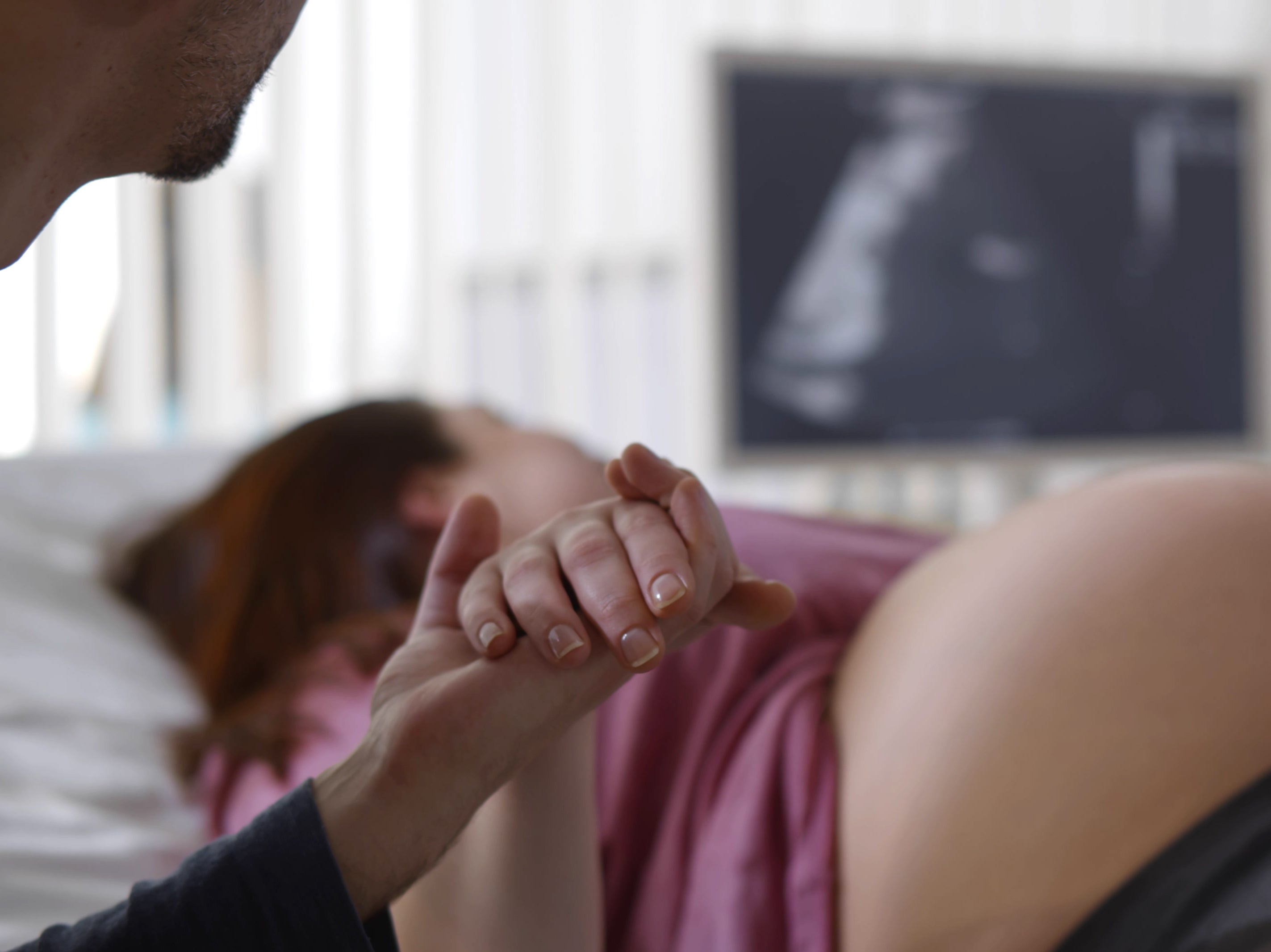 Close-up of a man holding pregnant wife’s hand during sonogram scanning in a clinic ( Getty Images )