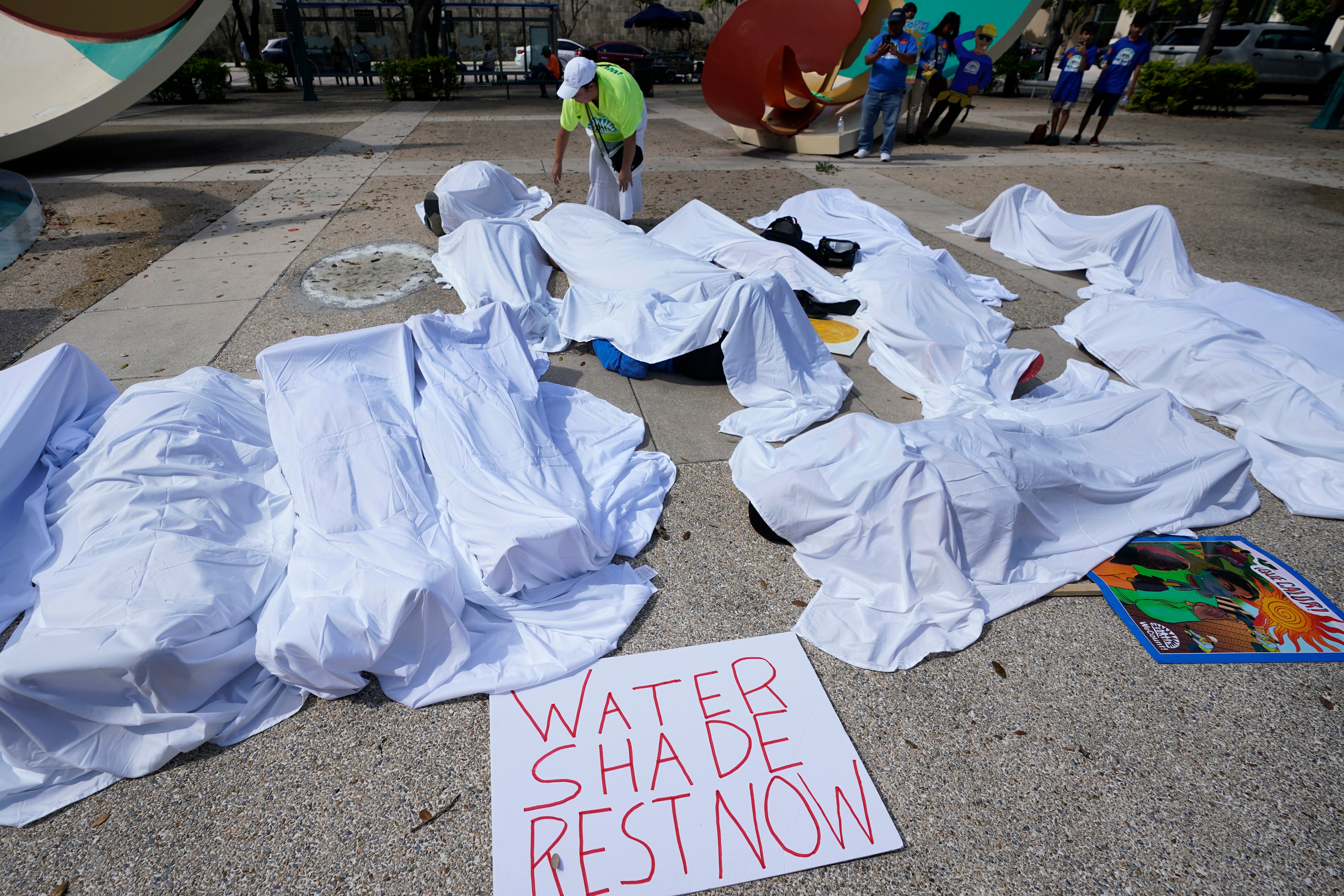 Activists cover themselves with sheets to simulate workers killed by extreme heat in the USA