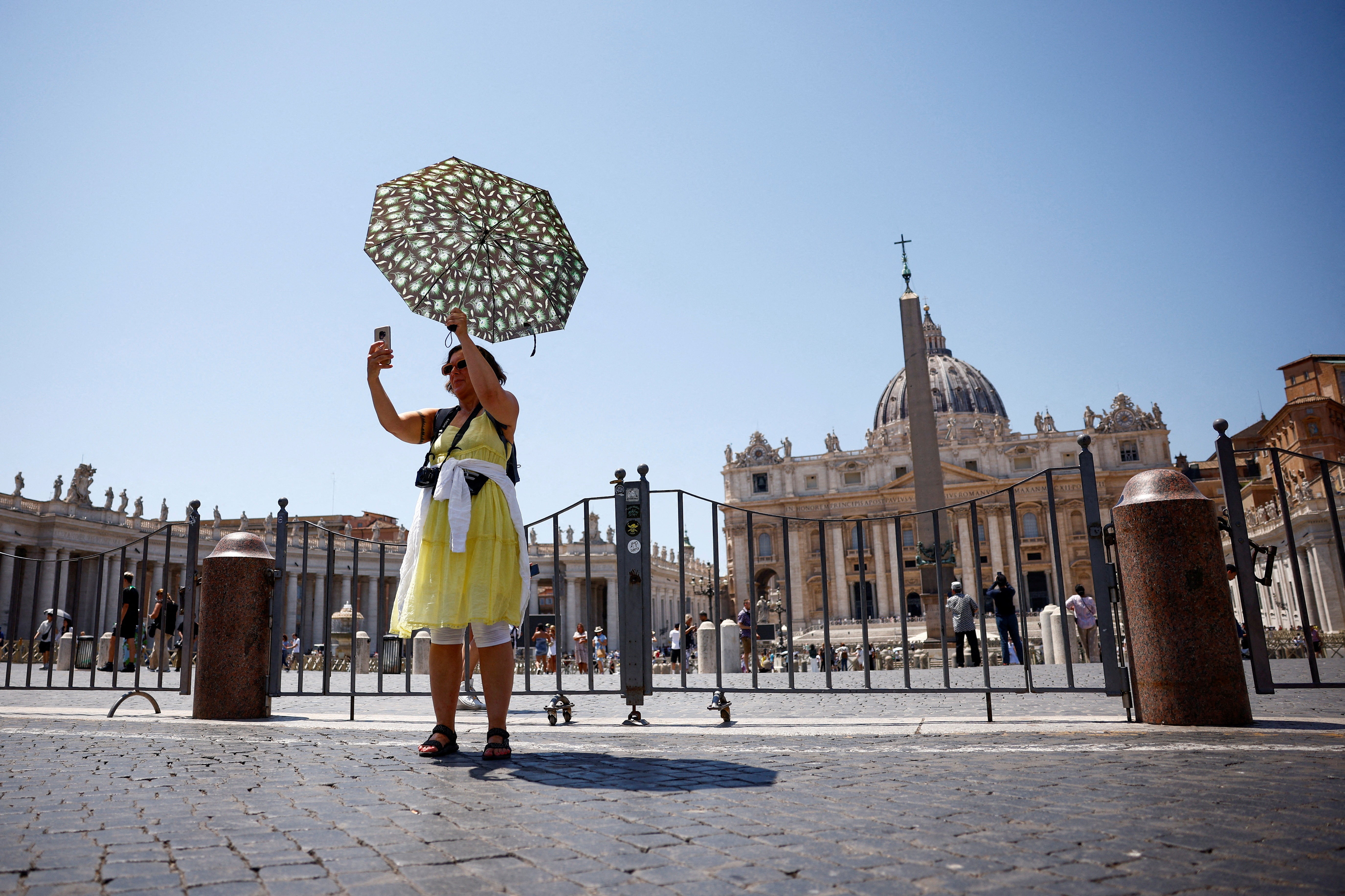 A woman takes a selfie as she shelters from the sun with an umbrella near St Peter's Square during a heatwave in Rome, Italy