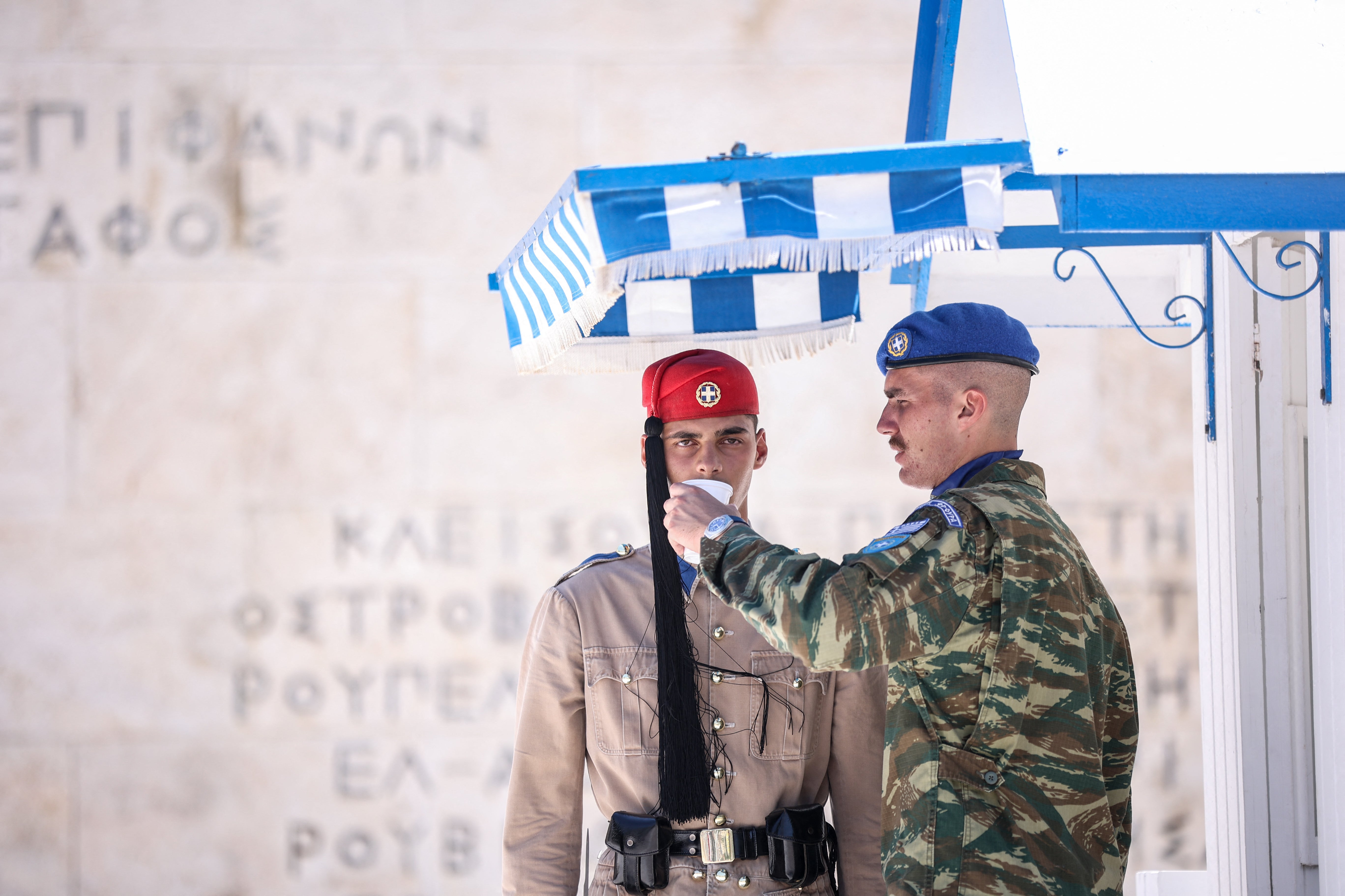 An officer gives water to a presidential guard member standing in front of the monument of The Unknown Soldier in Syntagma Square in Athens on July 12, 2024