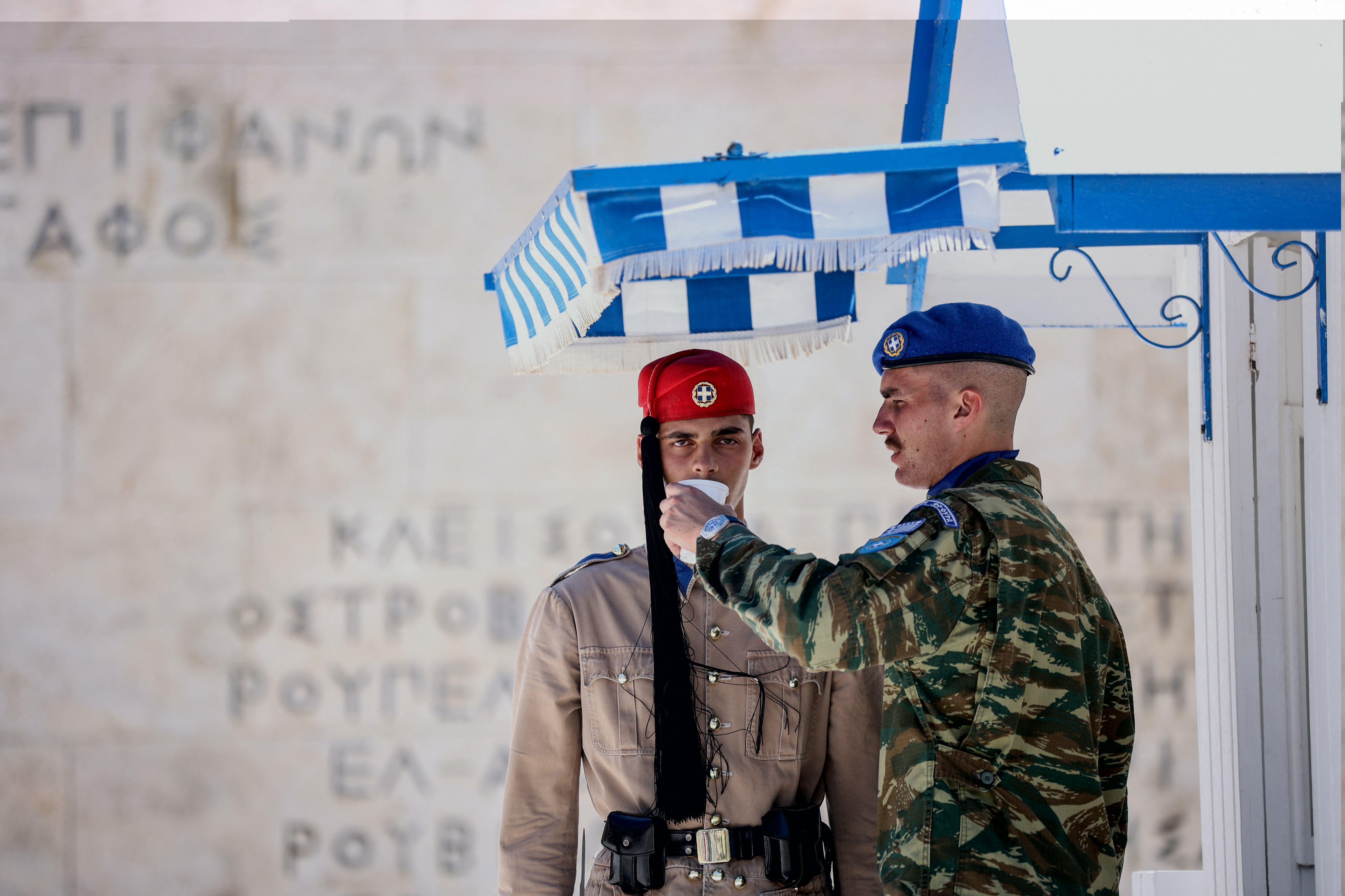 An officer gives water to a presidential guard member standing in front of the monument of The Unknown Soldier in Syntagma Square in Athens on 12 July, 2024