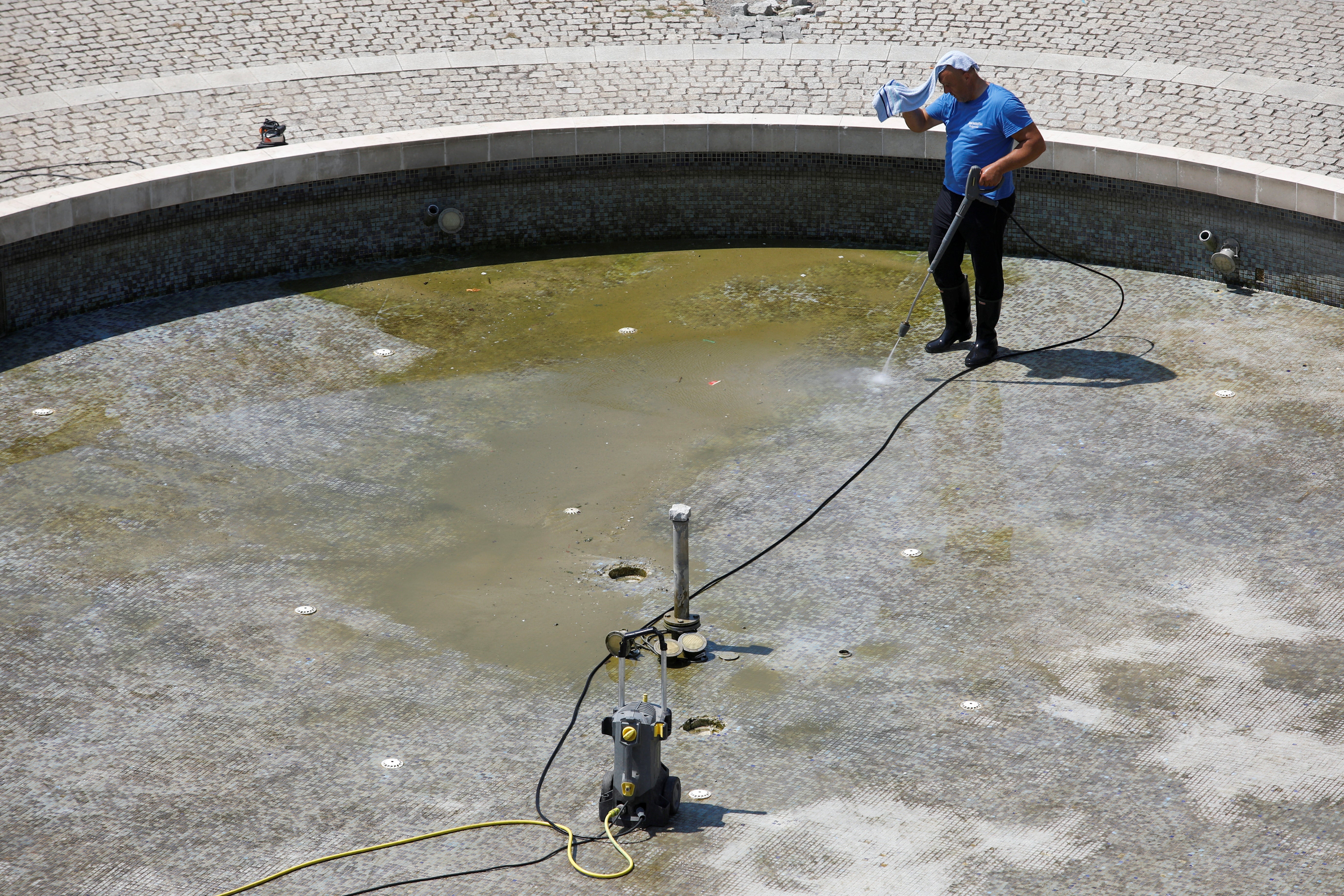 A worker put a wet towel on his head to protect himself from the heat while cleaning a fountain in downtown Podgorica, Montenegro