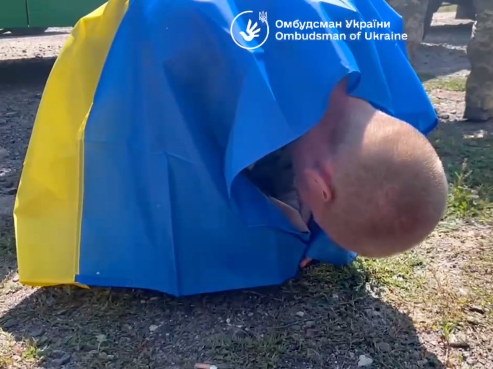 A soldier clutching a Ukraine flag collapses on the ground after arriving back in his home country