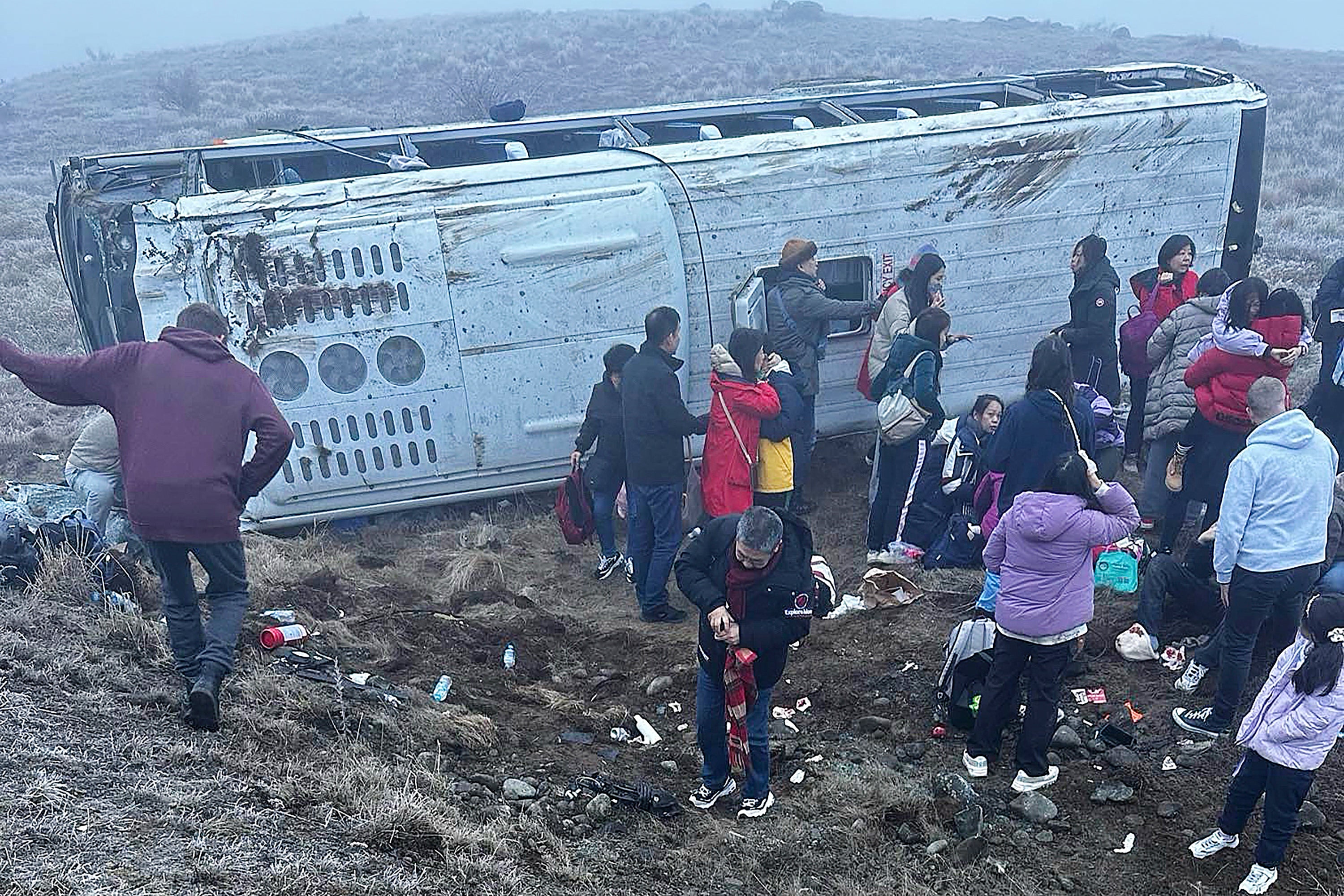 In this photo provided by Grace Duggin, people are in a ditch after a bus carrying Chinese tourists crashed near Lake Tekapo, New Zealand, on Thursday, July 18, 2024