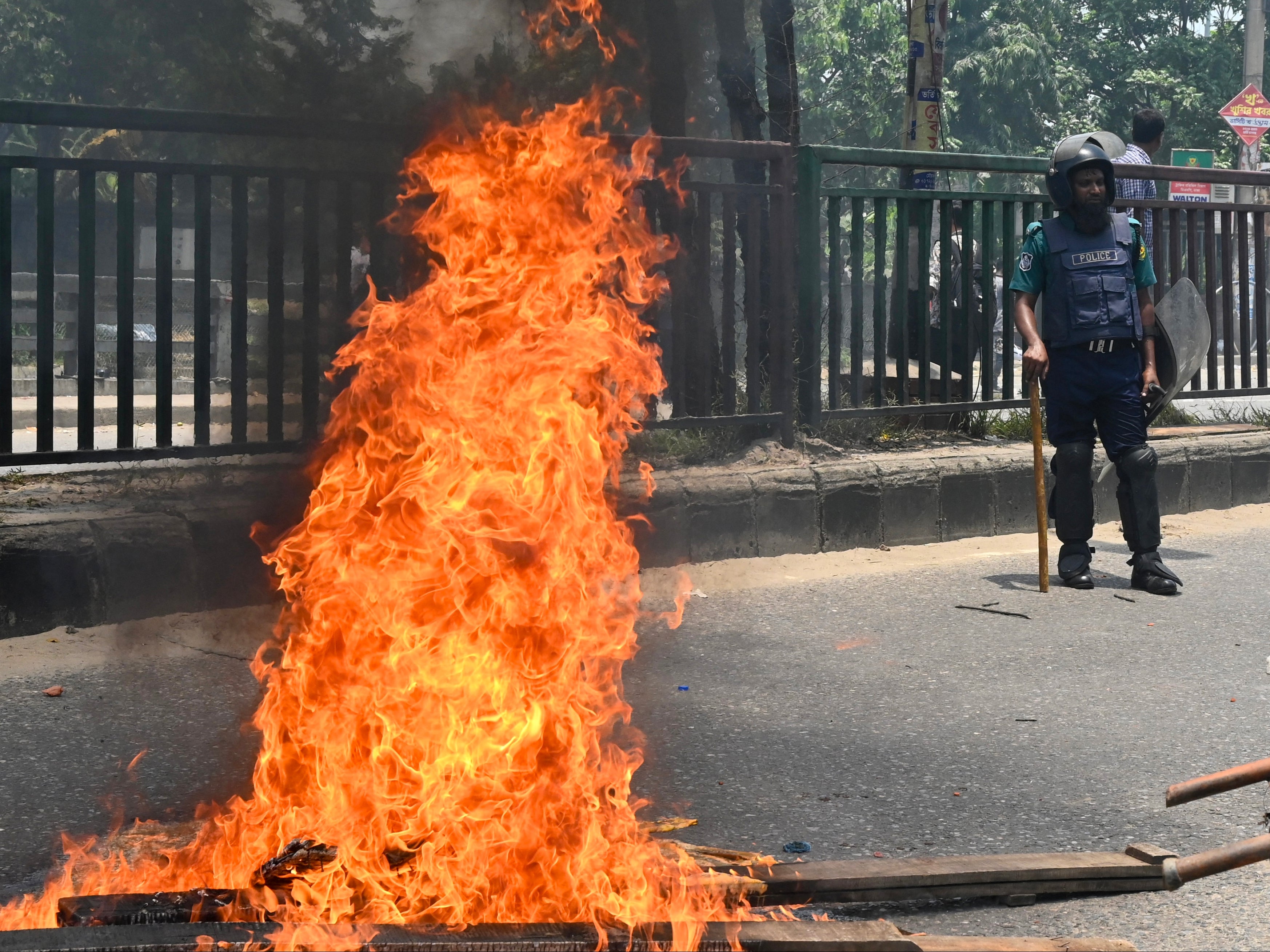 A policeman stands near a fire set by protesters during a clash in Dhaka on 18 July 2024