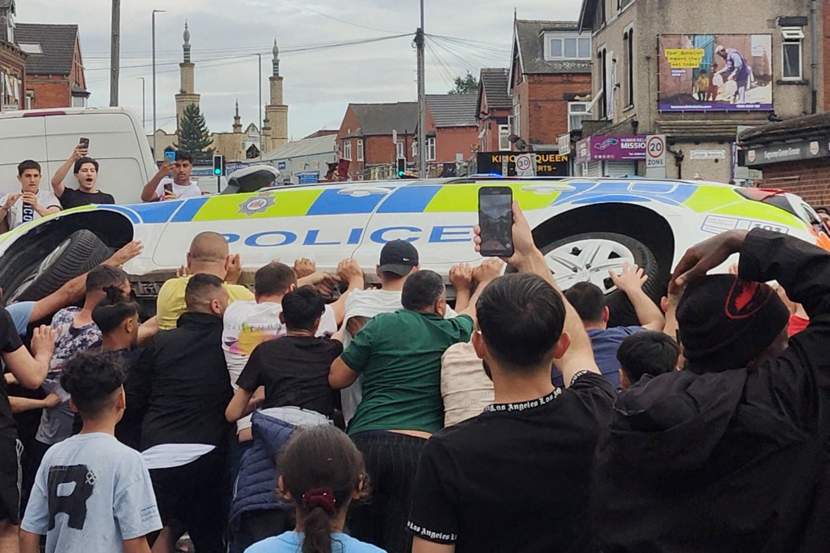 People overturn a police vehicle during unrest in Harehills