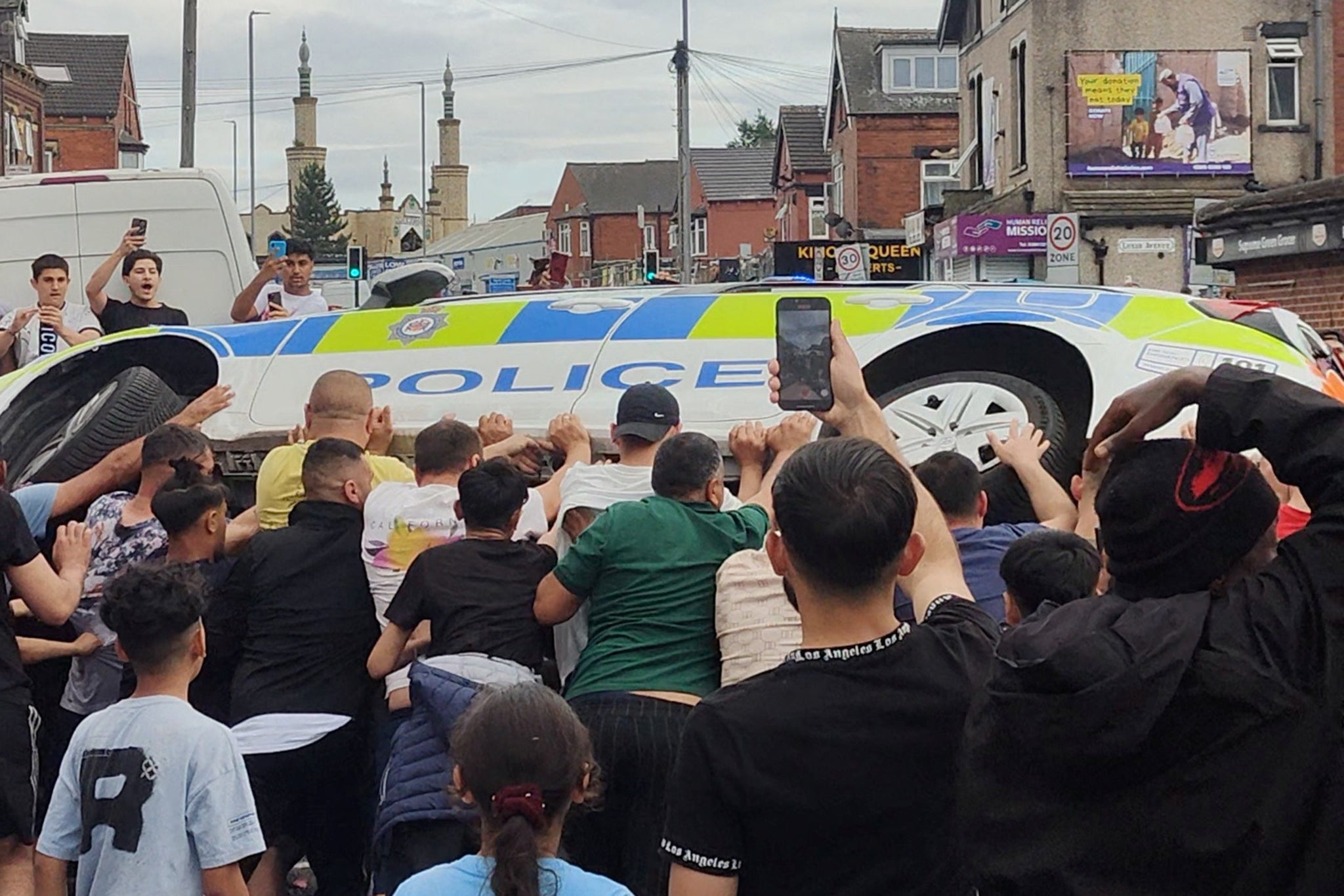 People overturn a police vehicle during unrest in Harehills