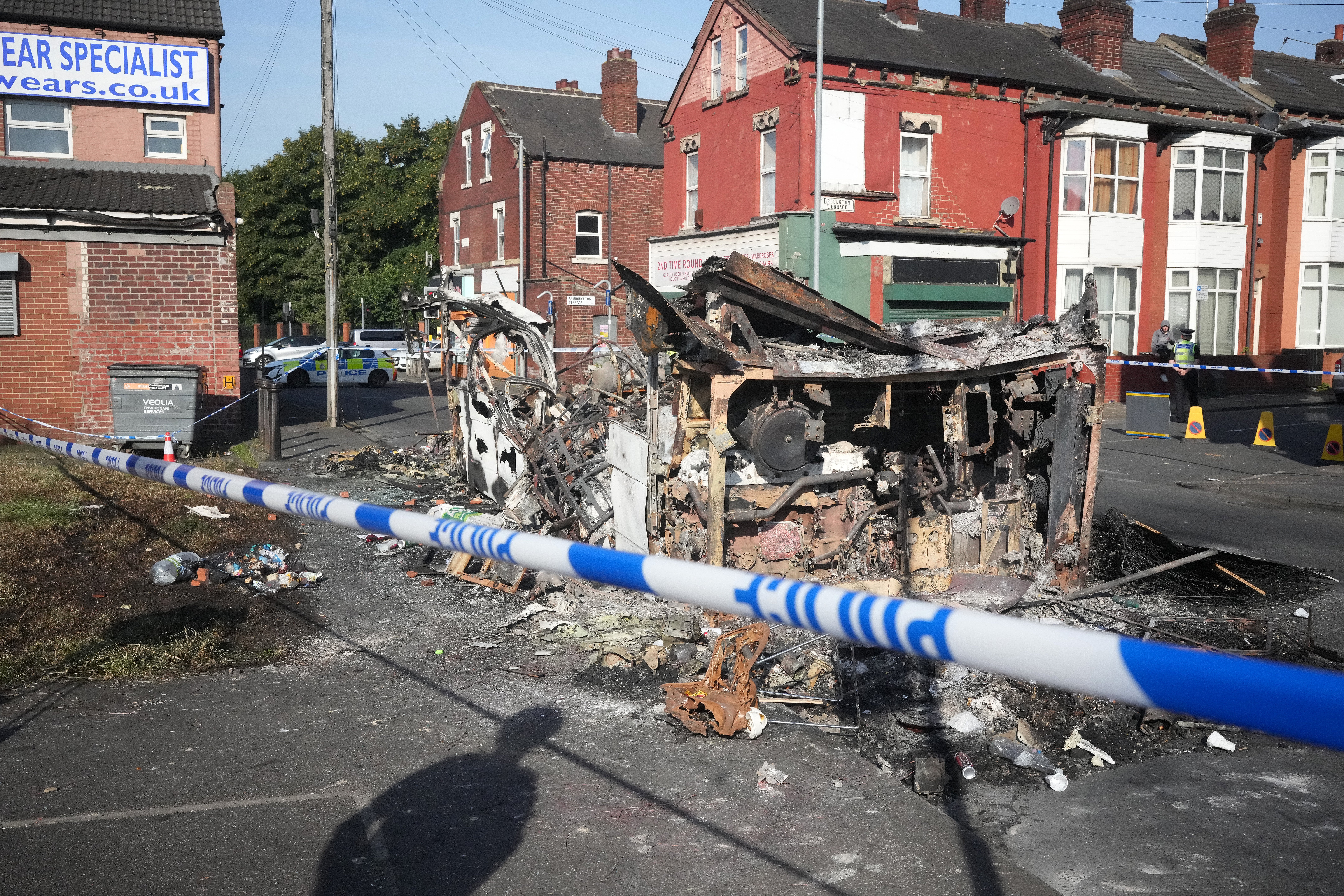 Police tape cordons off the remains of a burnt out bus after riots broke out in Leeds, West Yorkshire, on Thursday