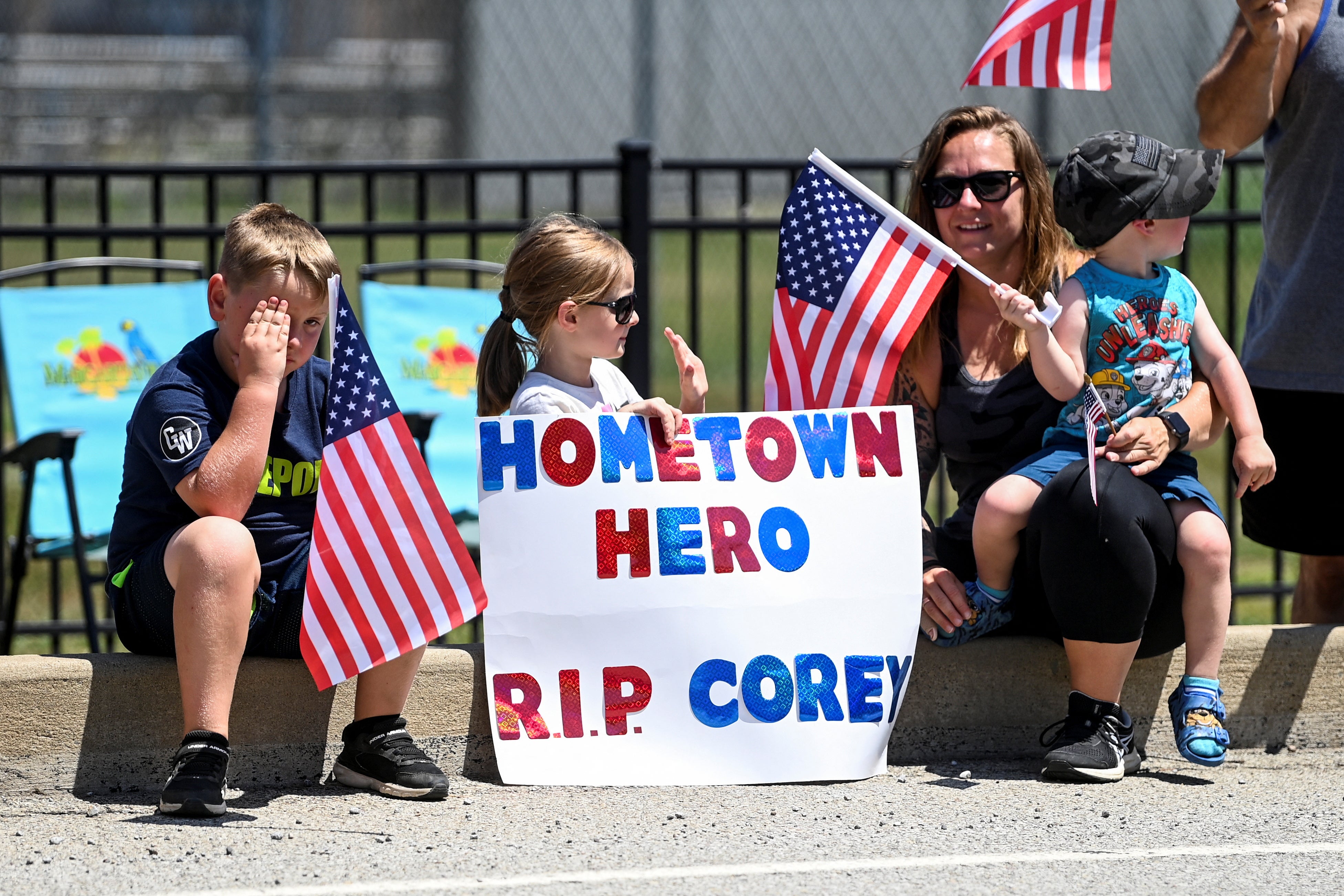 A girl holds a placard as people wait for a procession of emergency vehicles transporting the coffin