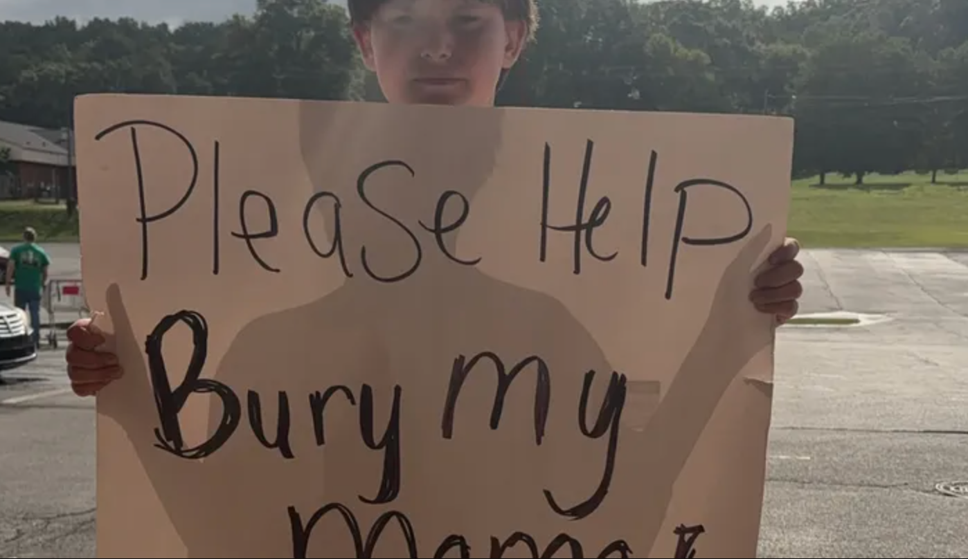 Eleven-year-old Kayden of Lindale, Georgia, holds a sign that reads, “Please help bury my Mama!" and stood by railroad tracks for days asking for assistance