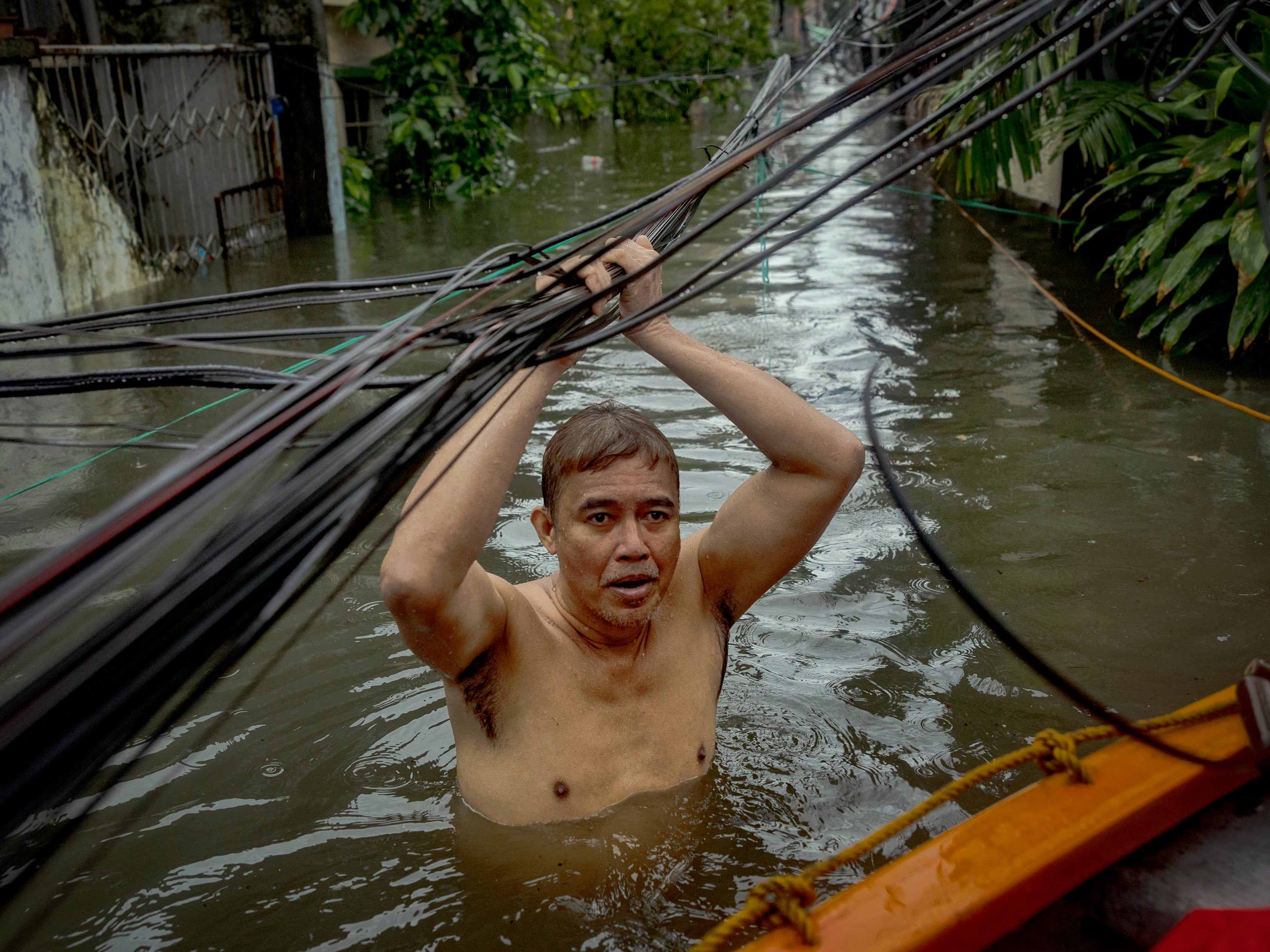 A man holds on to power lines as he wades floodwaters in Quezon city, Philippines