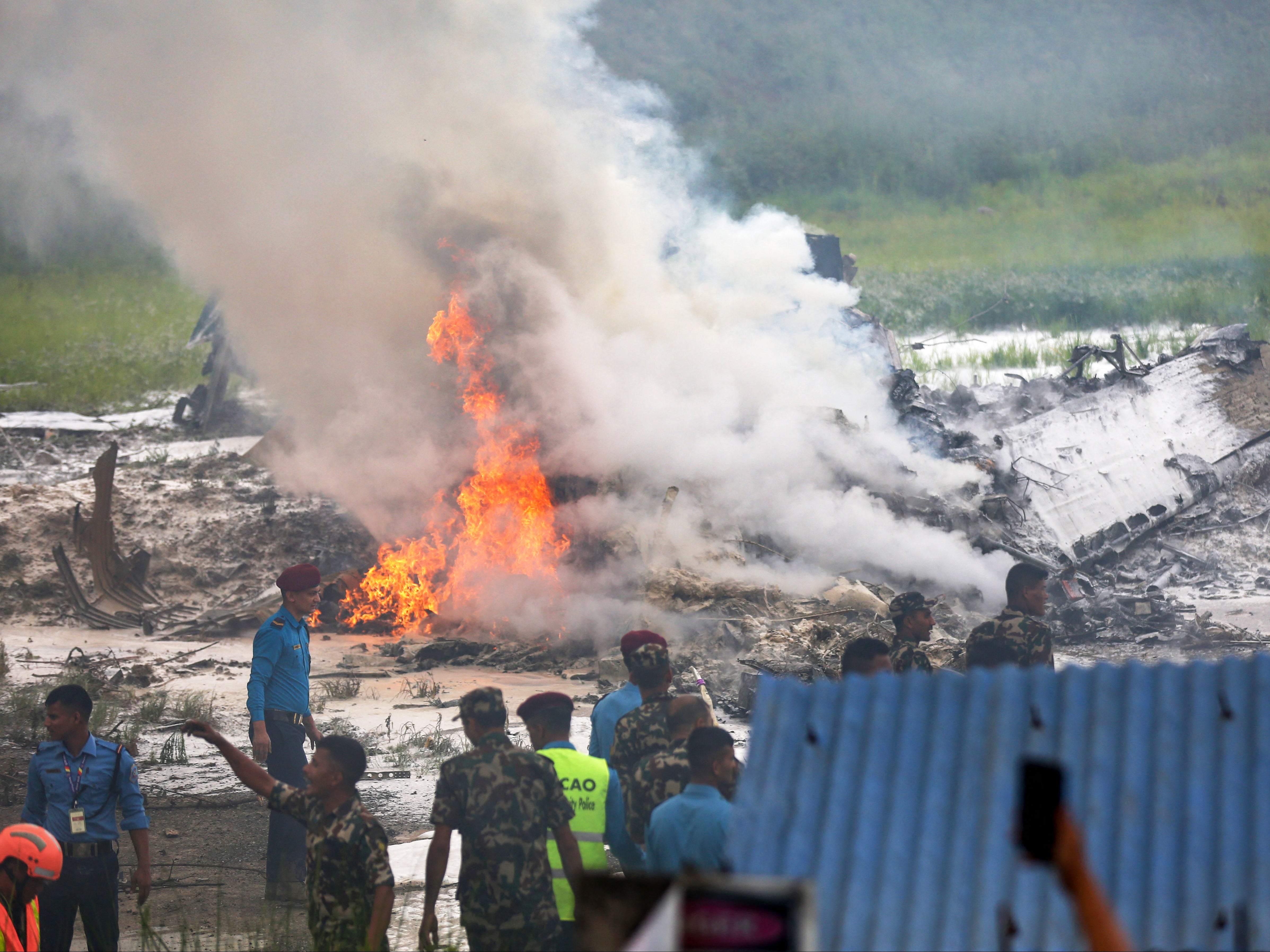 Security personnel gather near the burning Saurya Airlines flight after it crashed