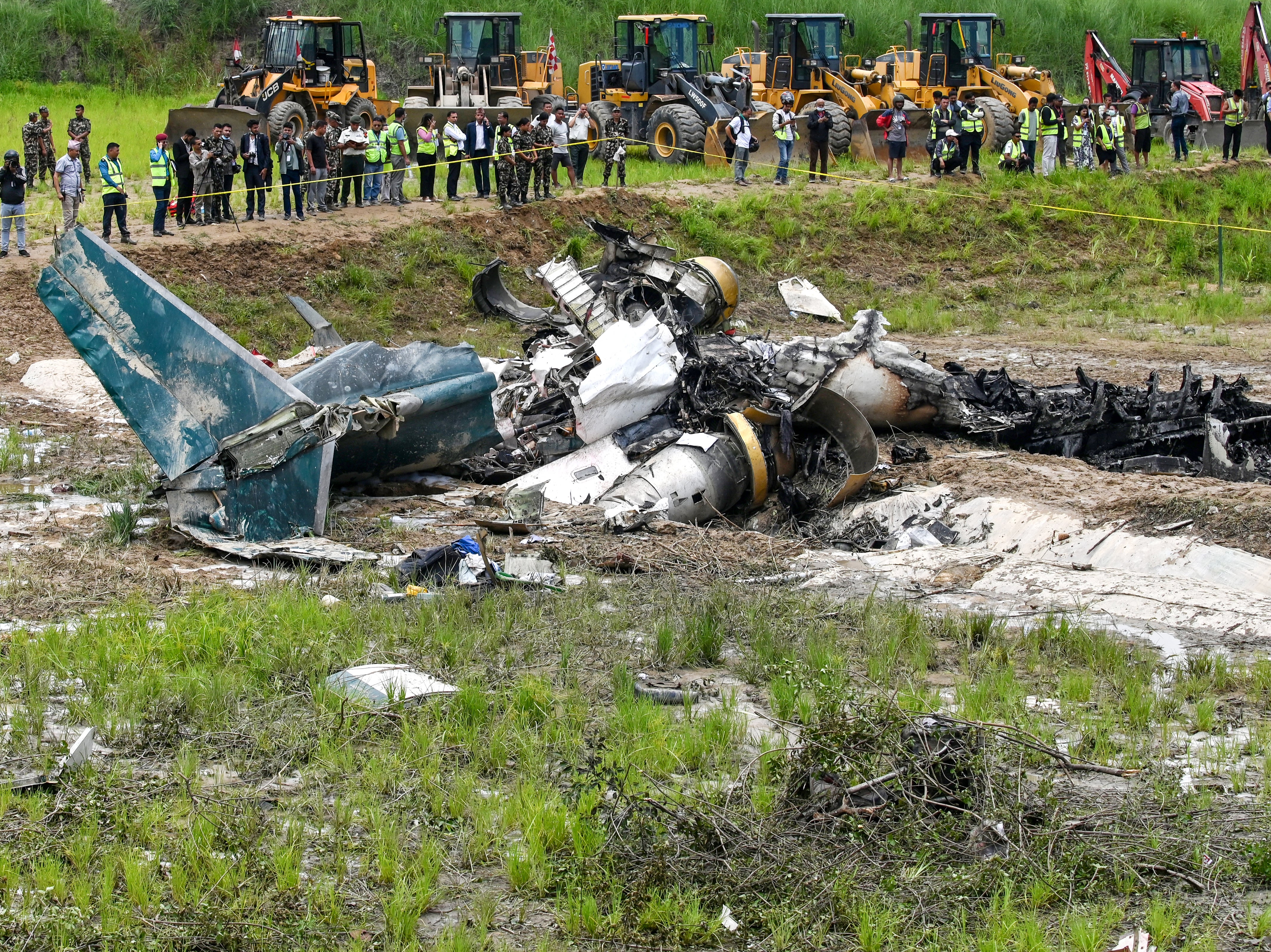 Army personnel and other officials stand around the debris of a Saurya Airlines flight after it crashed during takeoff at Tribhuvan International Airport in Kathmandu on 24 July 2024