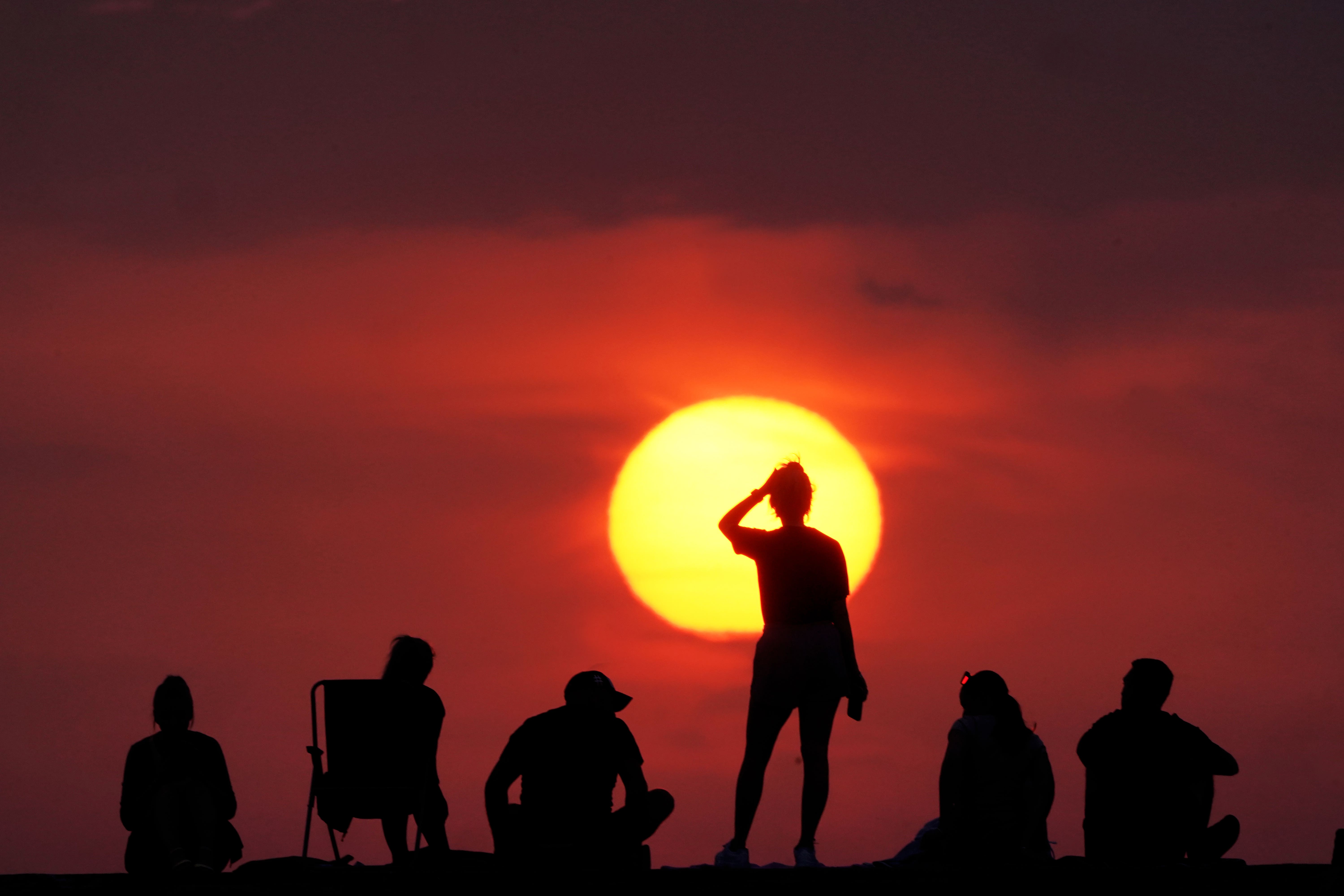 People watcing the sunrise at Cullercoats Bay, North Tyneside on what became the UK’s hottest day on record (Owen Humphreys/PA)