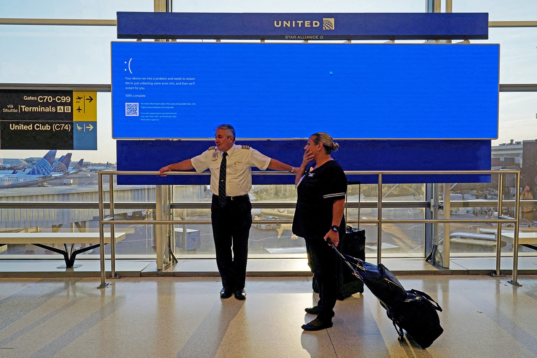 United Airlines employees wait by a monitor displaying the ‘blue screen of death’