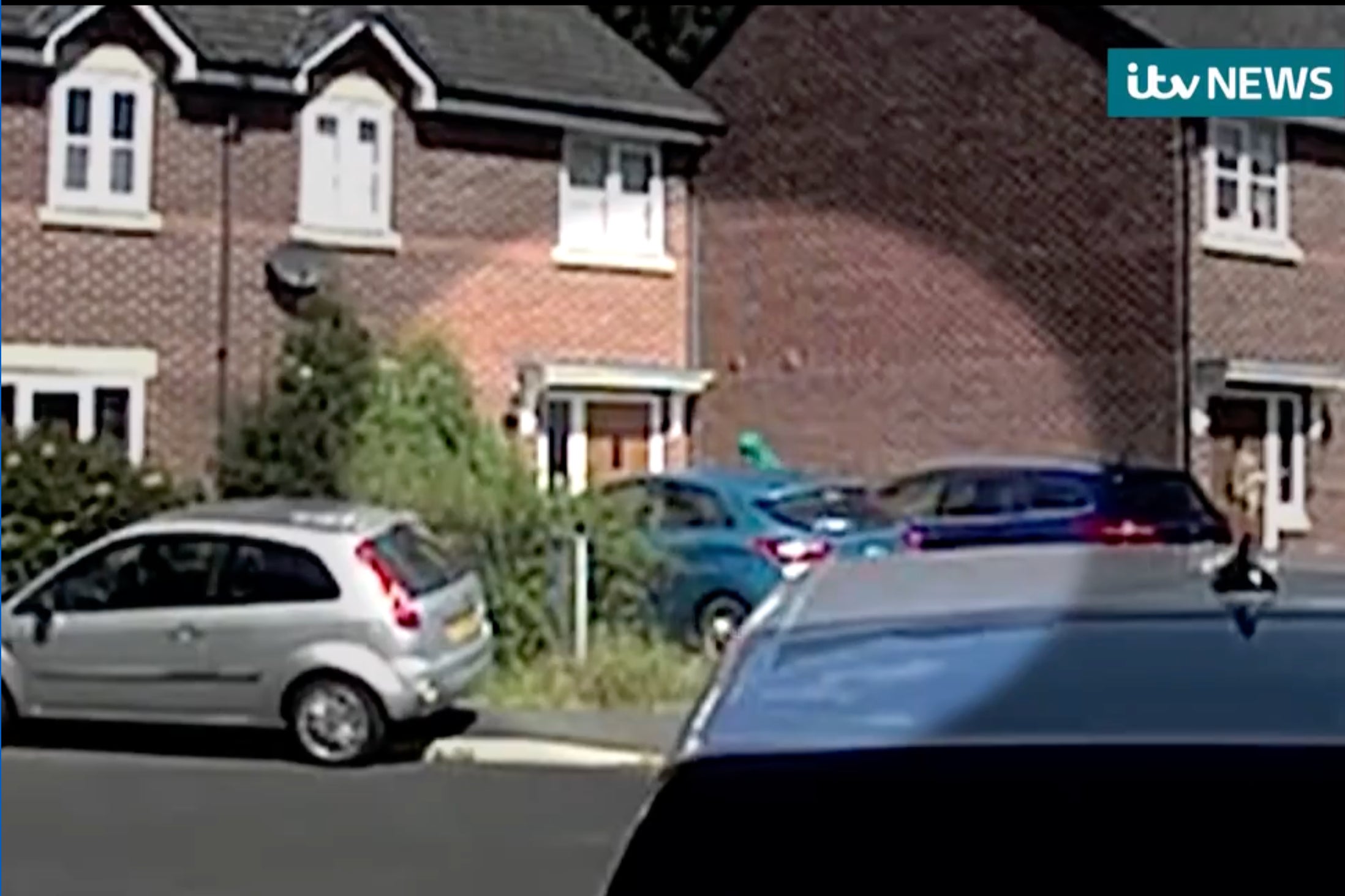 A person in a green hood and face mask circles a house