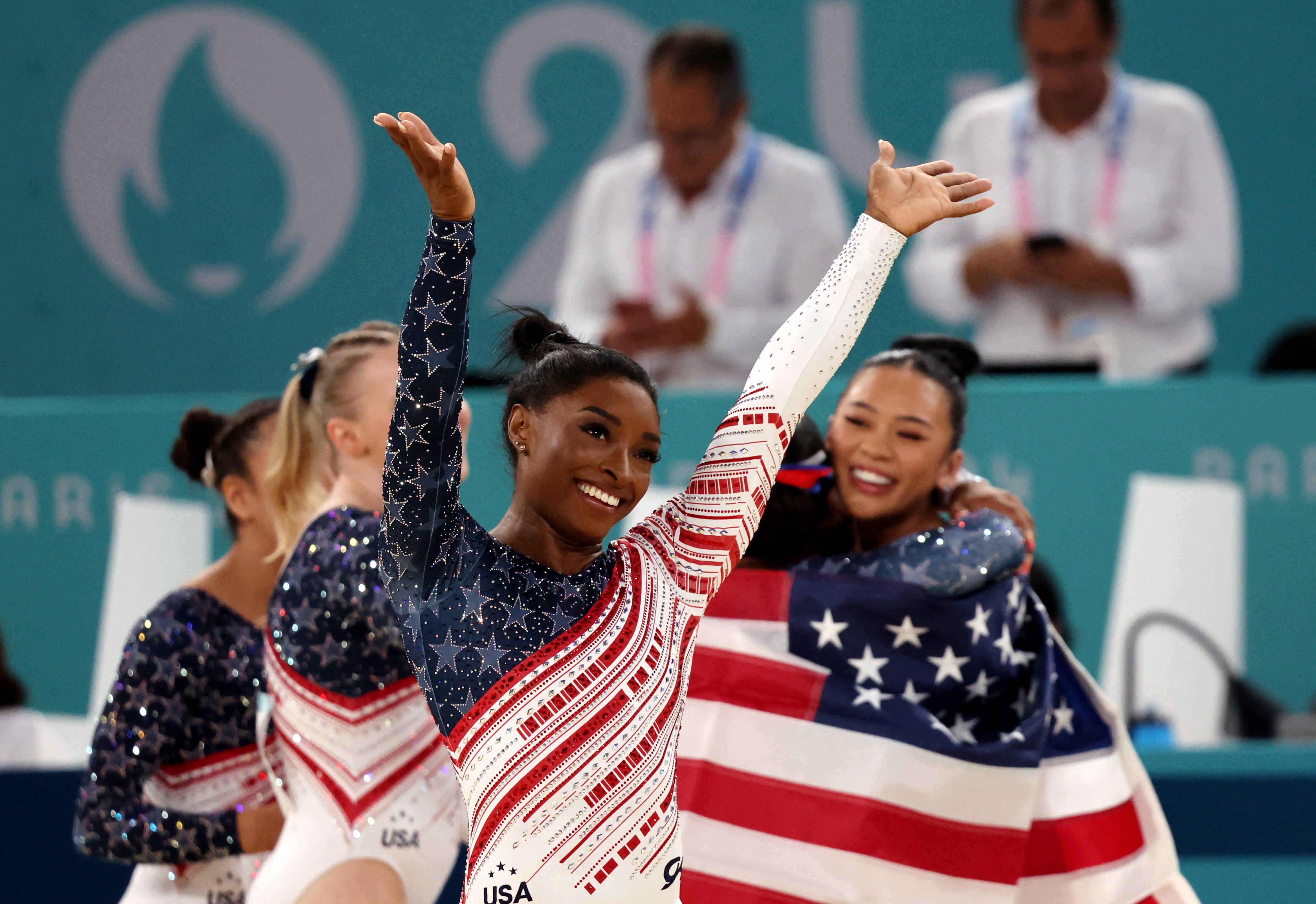 Simone Biles salutes the American fans as her teammates celebrate