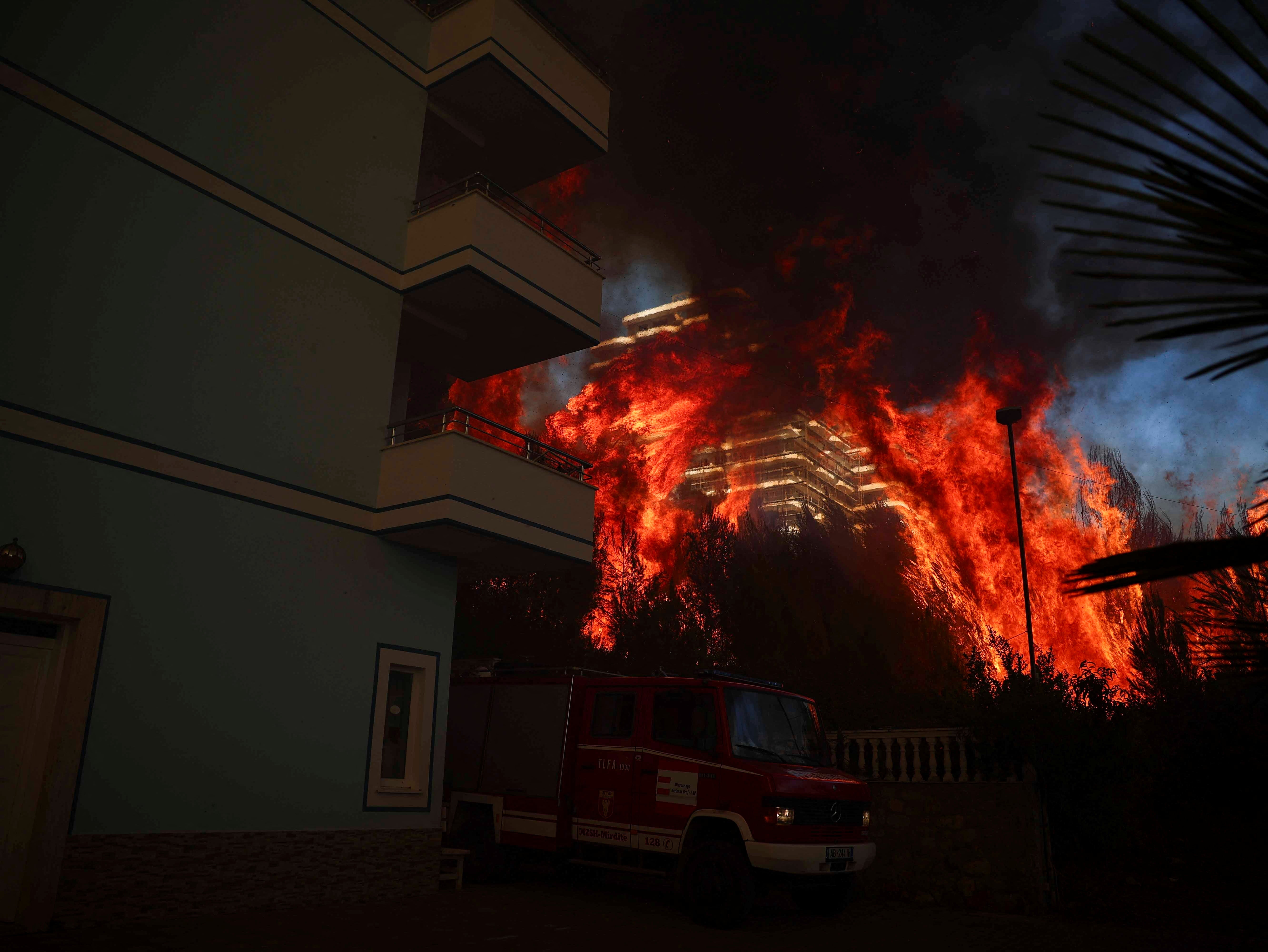 A firefighting vehicle stands parked, as members of emergency services work to contain a wildfire in Shengjin, Albania