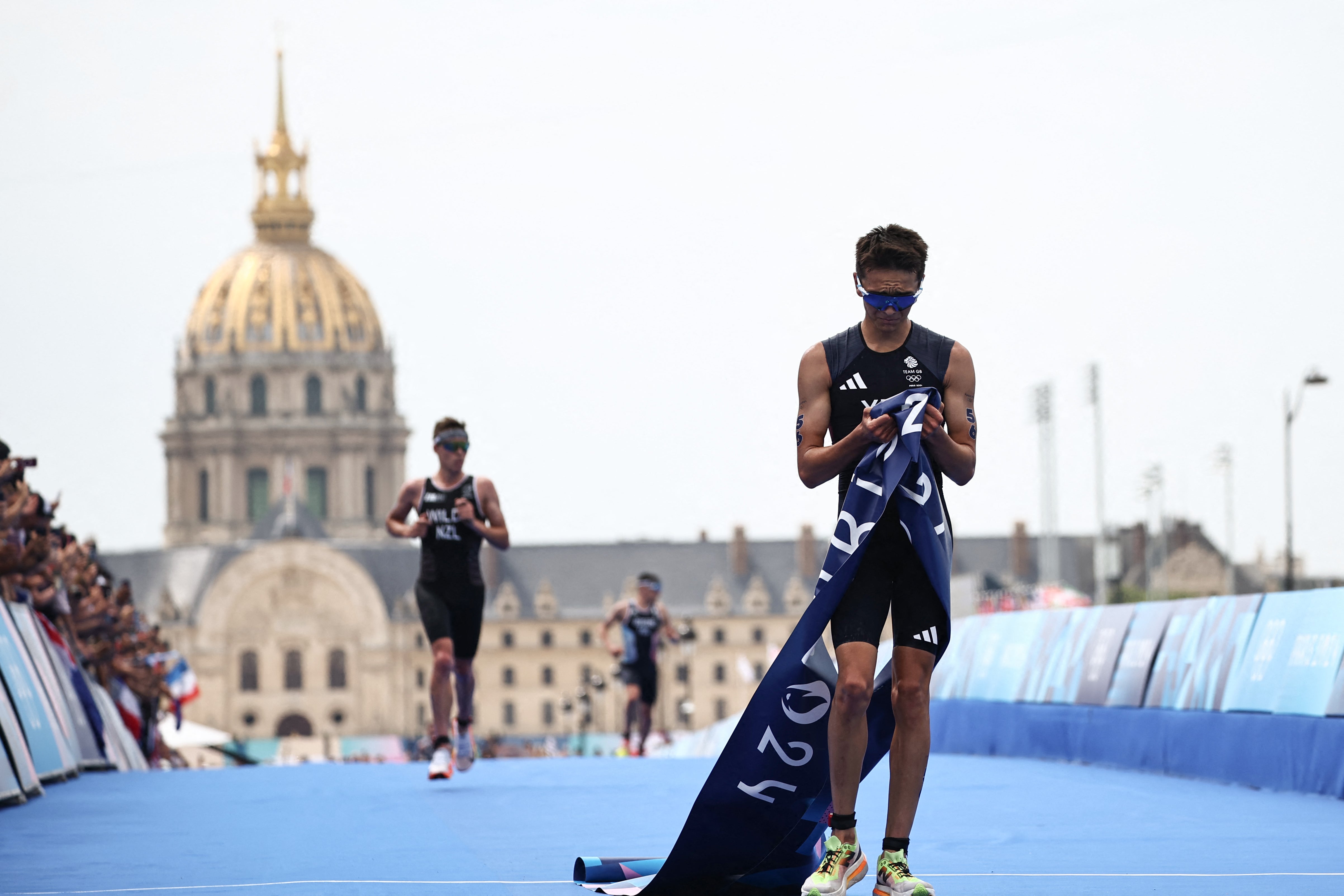 Alex Yee holds the finish tape in his hands after crossing the line for gold