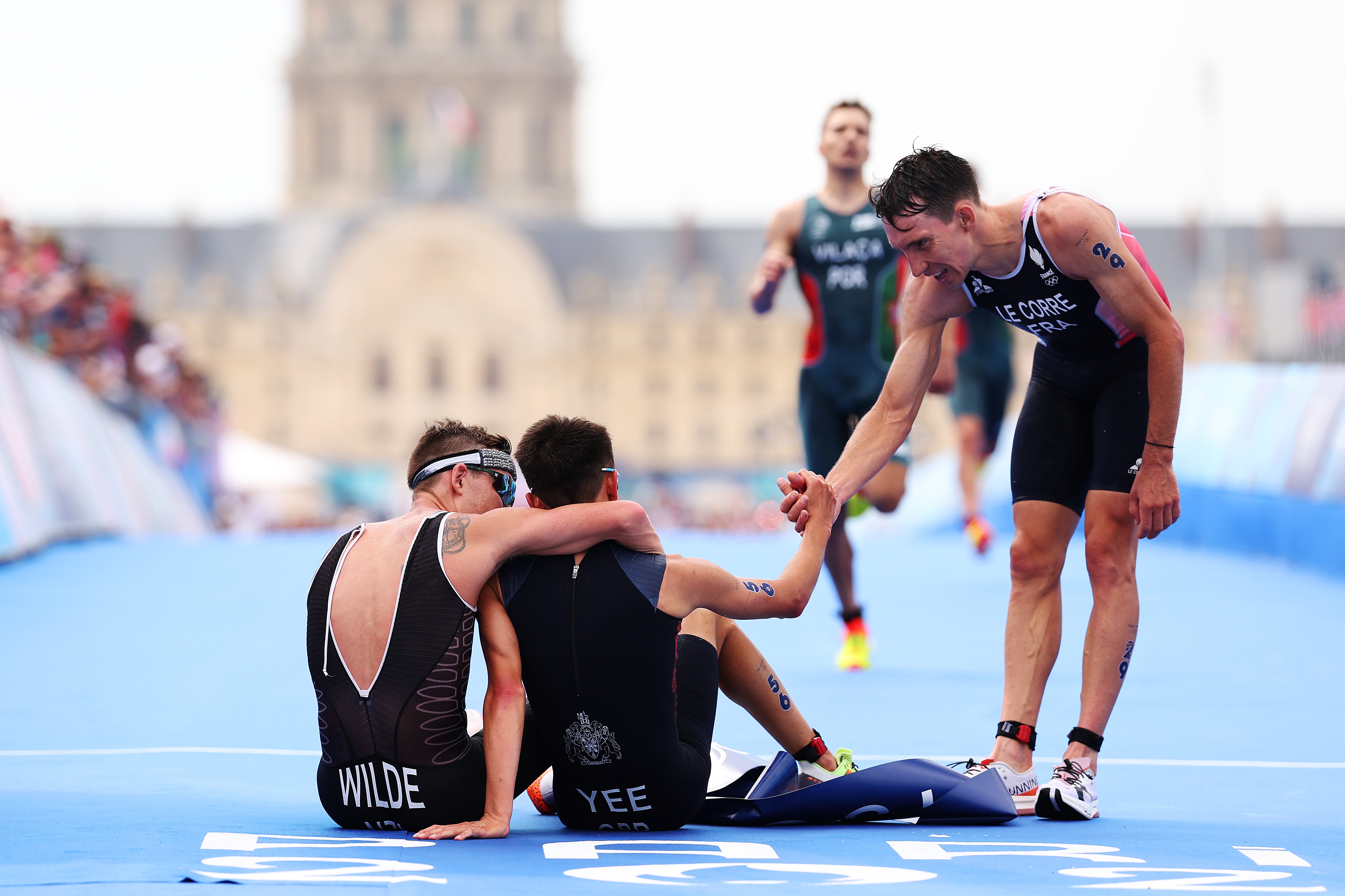 Hayden Wilde and Alex Yee, sitting on the finish line, are congratulated by Pierre le Corre