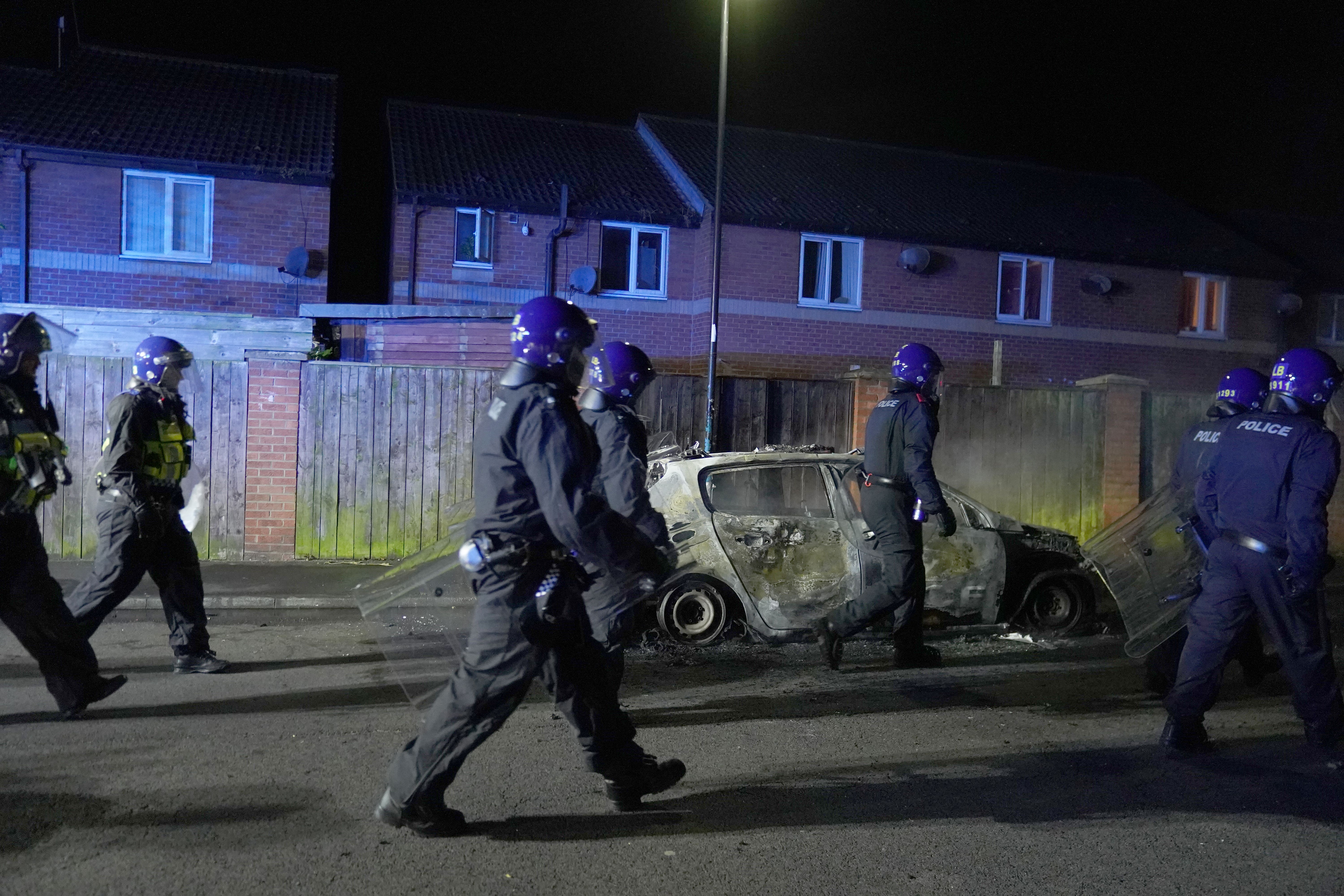 Police officers walk past a burnt-out police vehicle as they are deployed on the streets of Hartlepool following a violent protest on Wednesday (Owen Humphreys/PA)