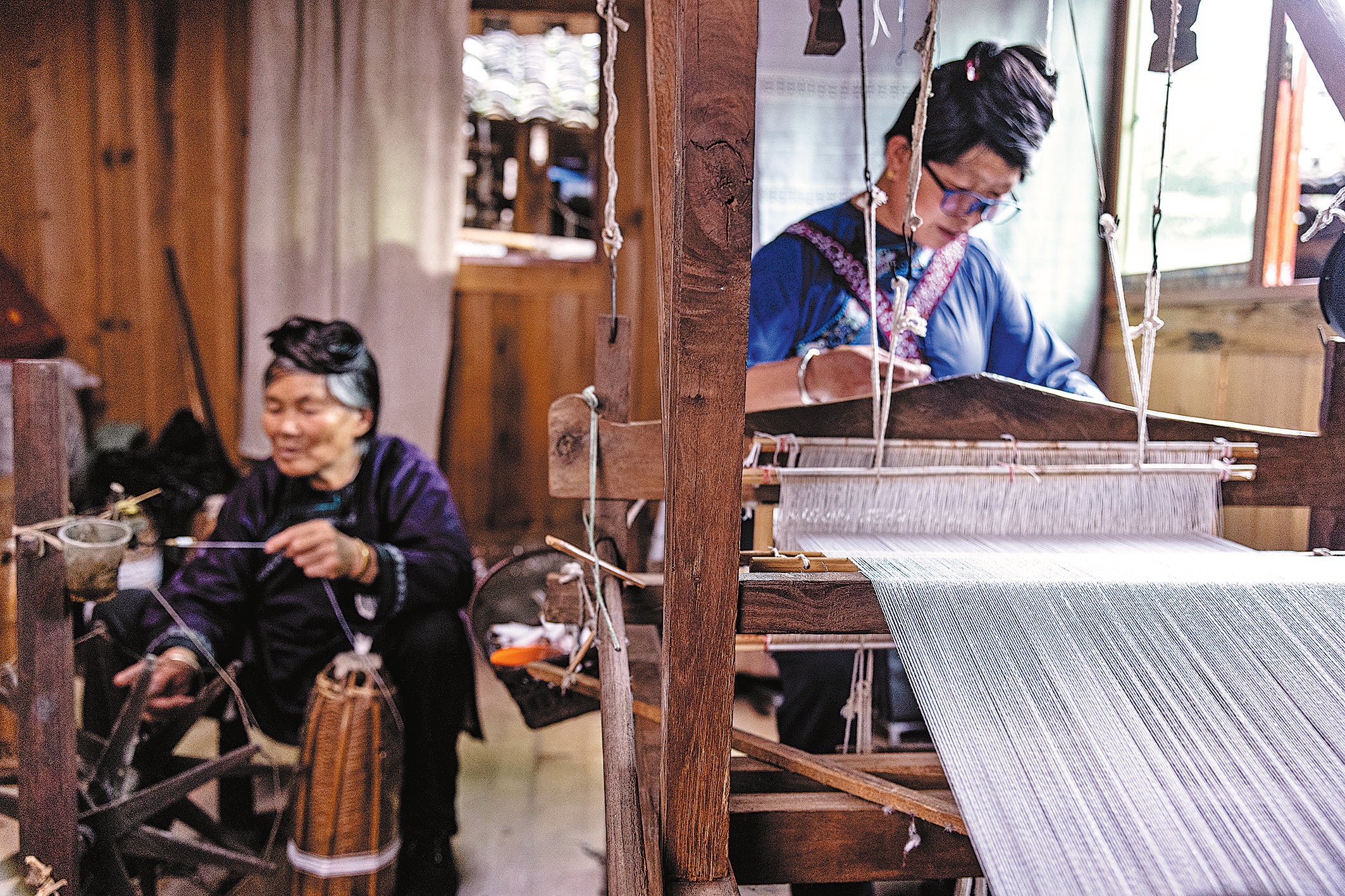 Yang Shenghua weaves Dong cloth on a loom, with her mother Yang Xiuying spinning threads by her side at their home in Dali Dong village, Rongjiang county, Guizhou province