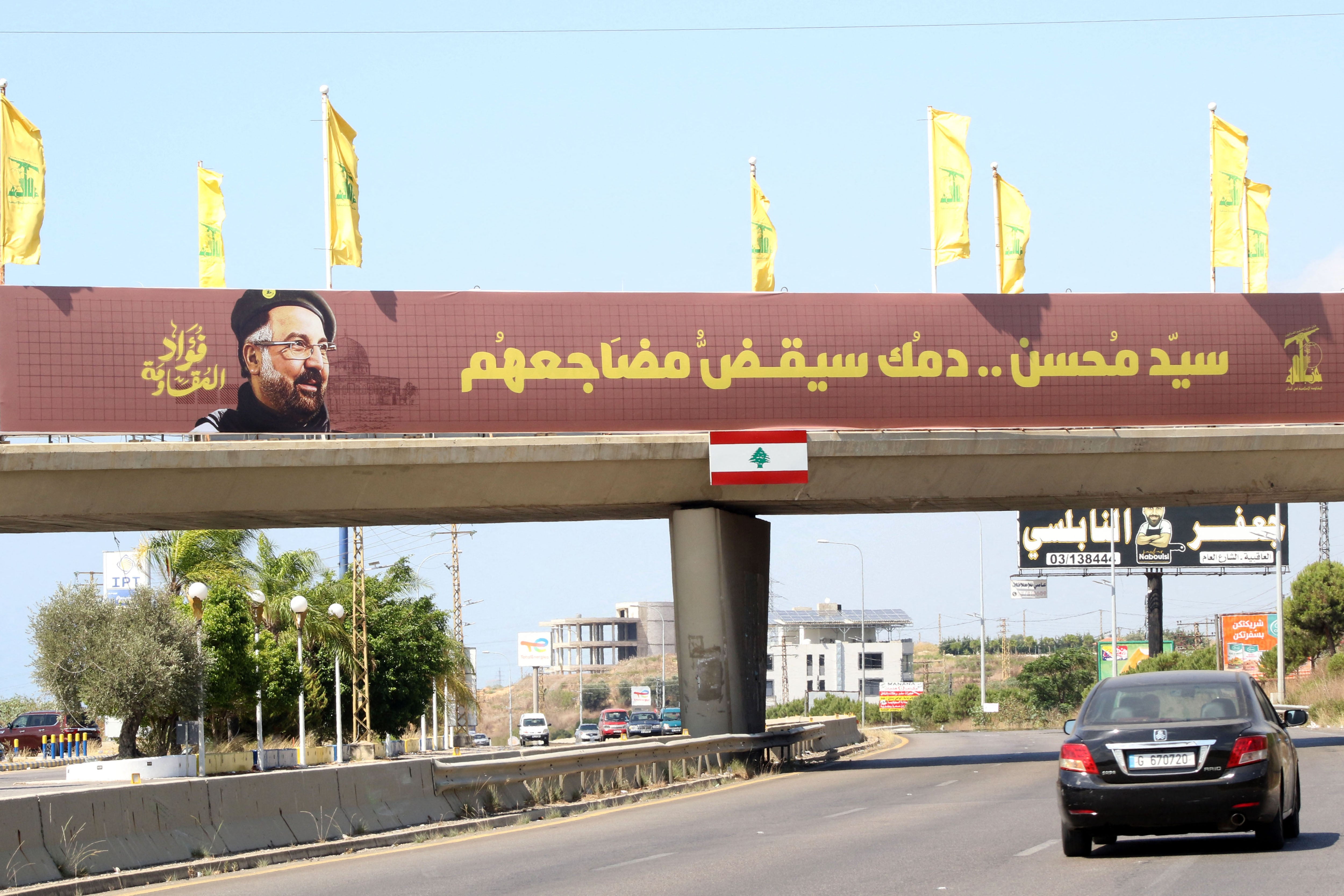 Yellow Hezbollah party flags fly alongside a banner showing the assassinated Hezbollah commander Fuad Shukr on a walkway on the Sidon to Tyre highway in southern Lebanon