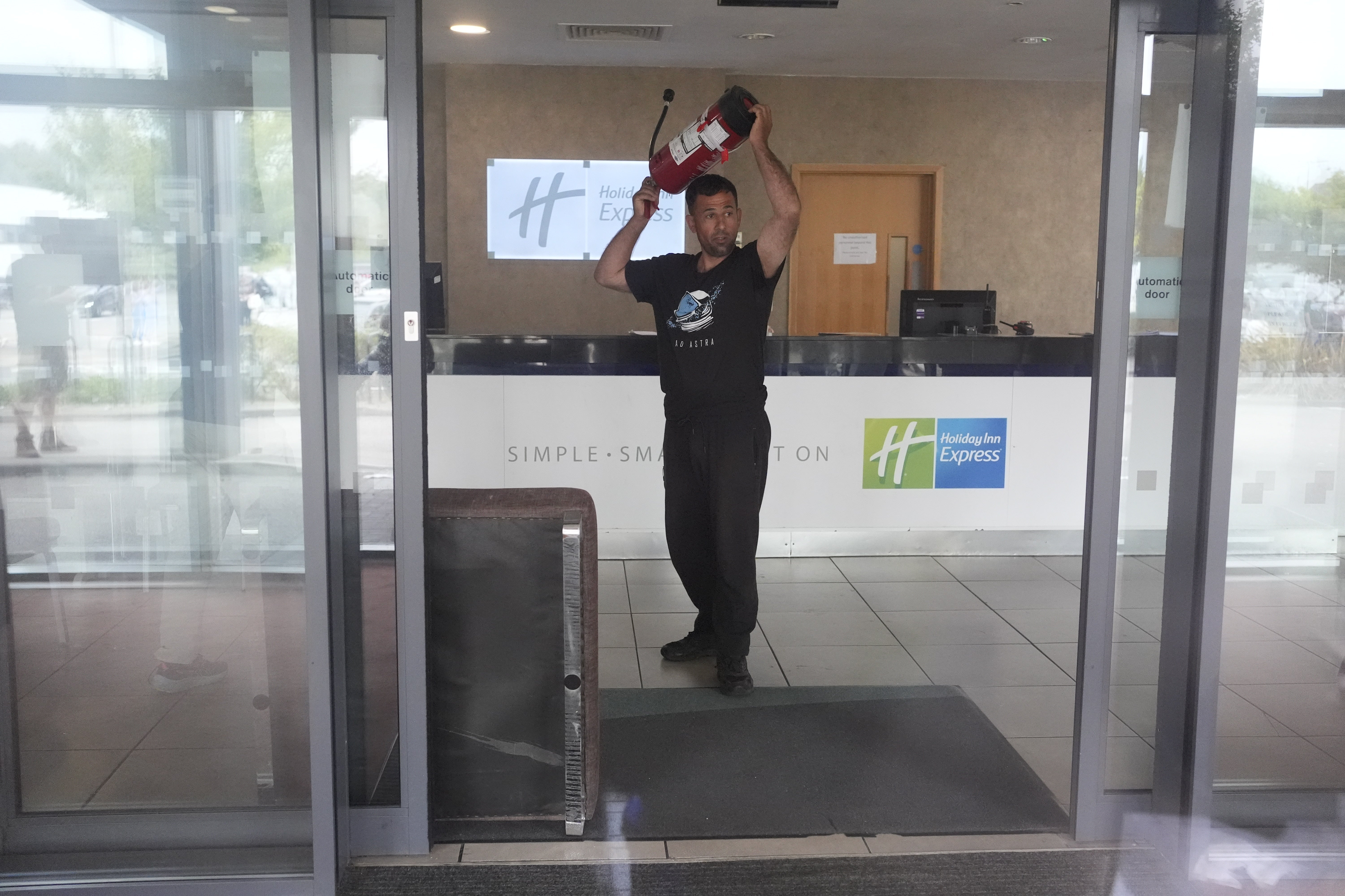 A man holds a fire extinguisher in the lobby of the hotel as seen through closed glass doors as trouble flares during an anti-immigration protest outside the Holiday Inn Express in Rotherham