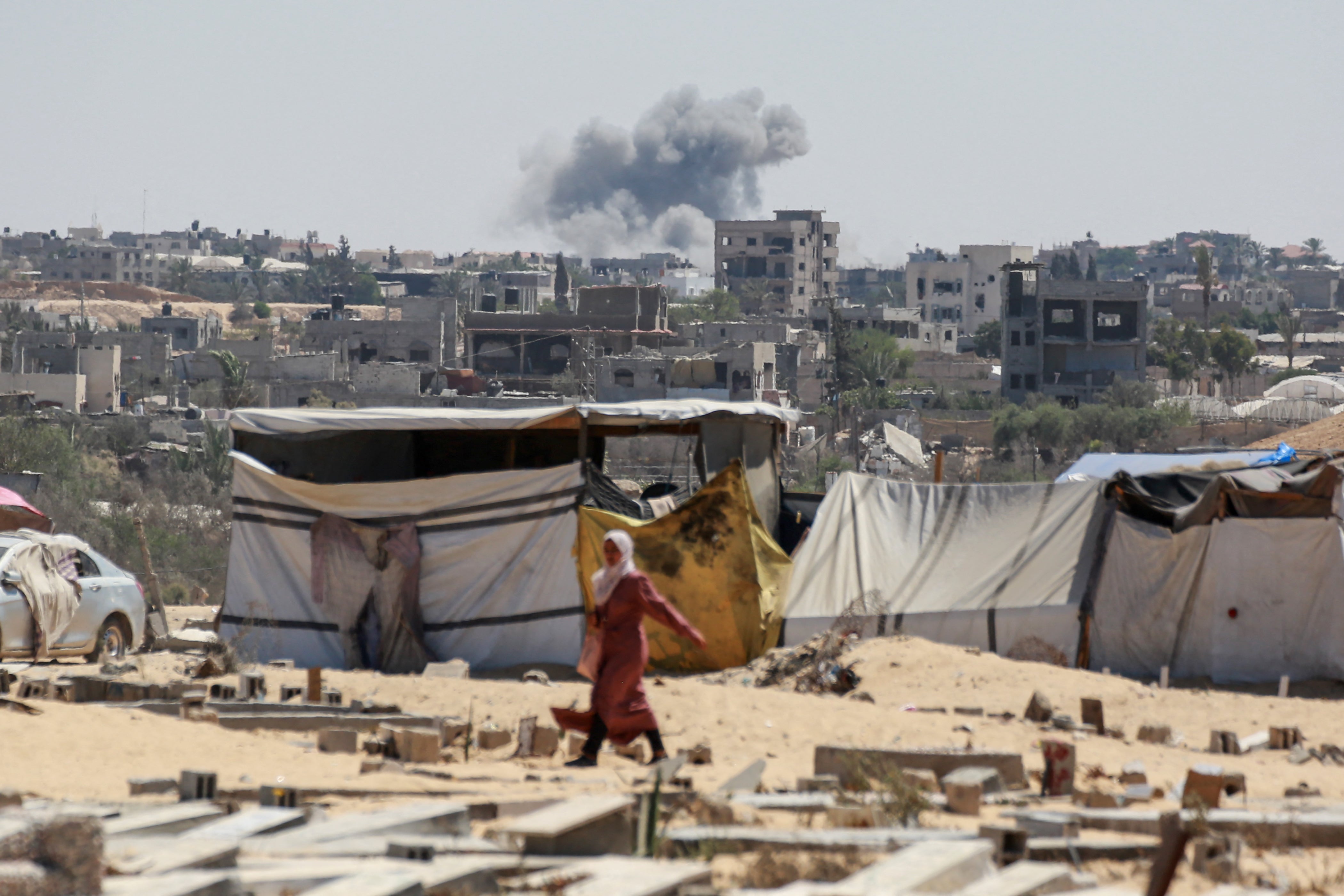 Smoke from Israeli bombardment billows in the background as a woman walks in Khan Yunis in the southern Gaza Strip on 5 August 2024