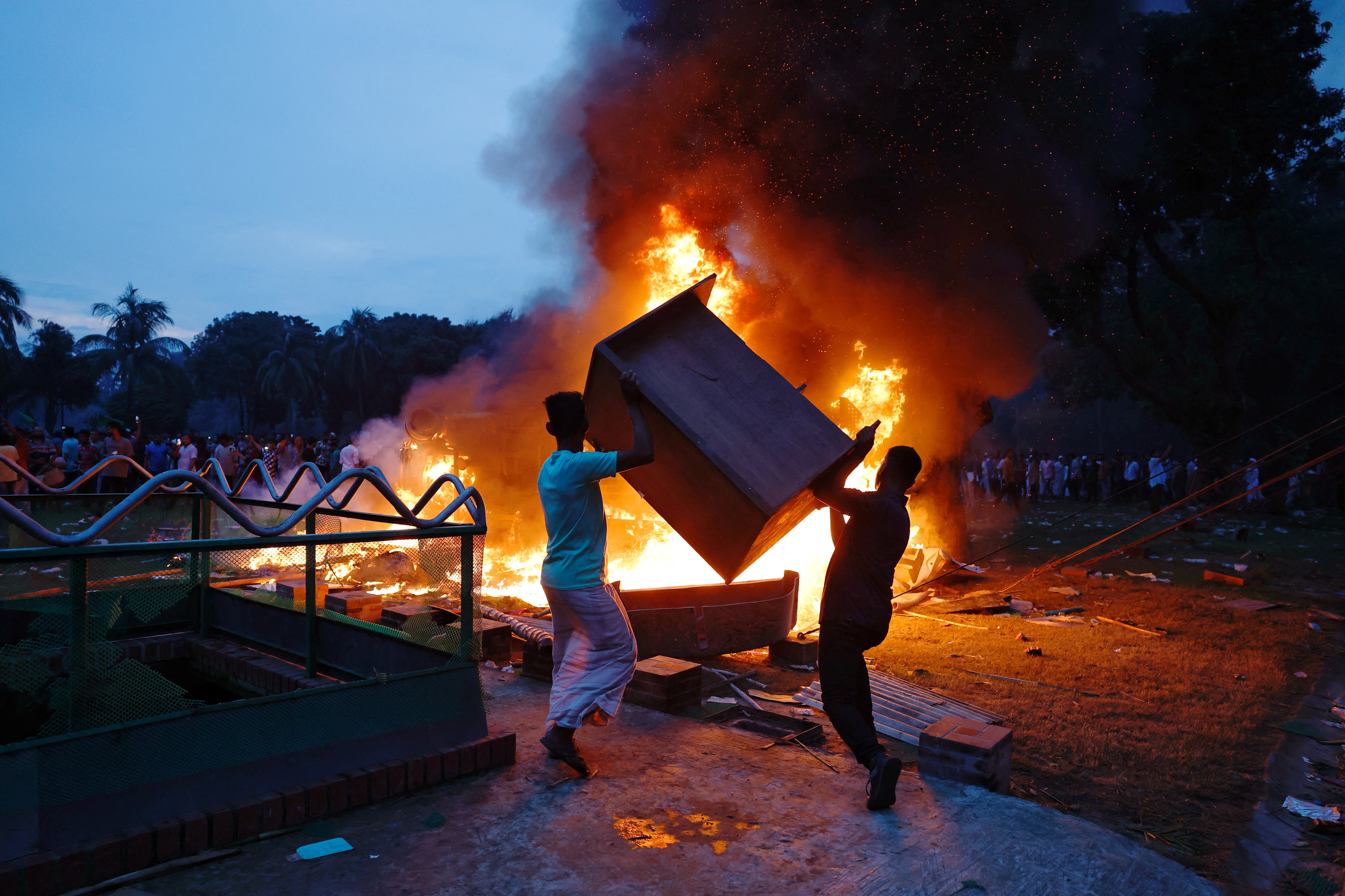 People throw wooden furniture into the fire that was set on a vehicle inside the Ganabhaban, the prime minister's residence, after the resignation of the Sheikh Hasina in Dhaka, Bangladesh