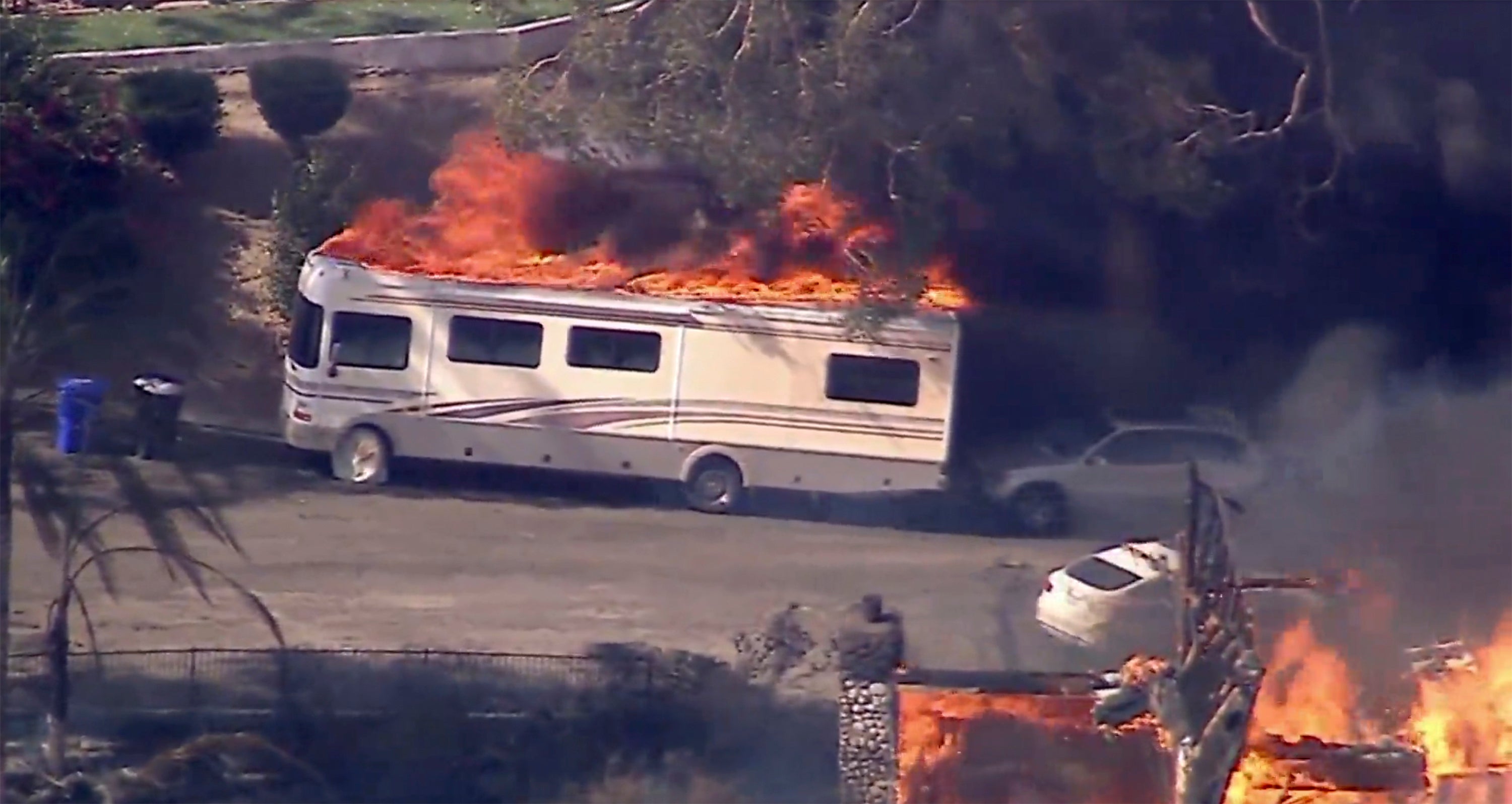 A camper catches fire as several homes burn as a fast-moving wildfire torched a California hillside community on Monday