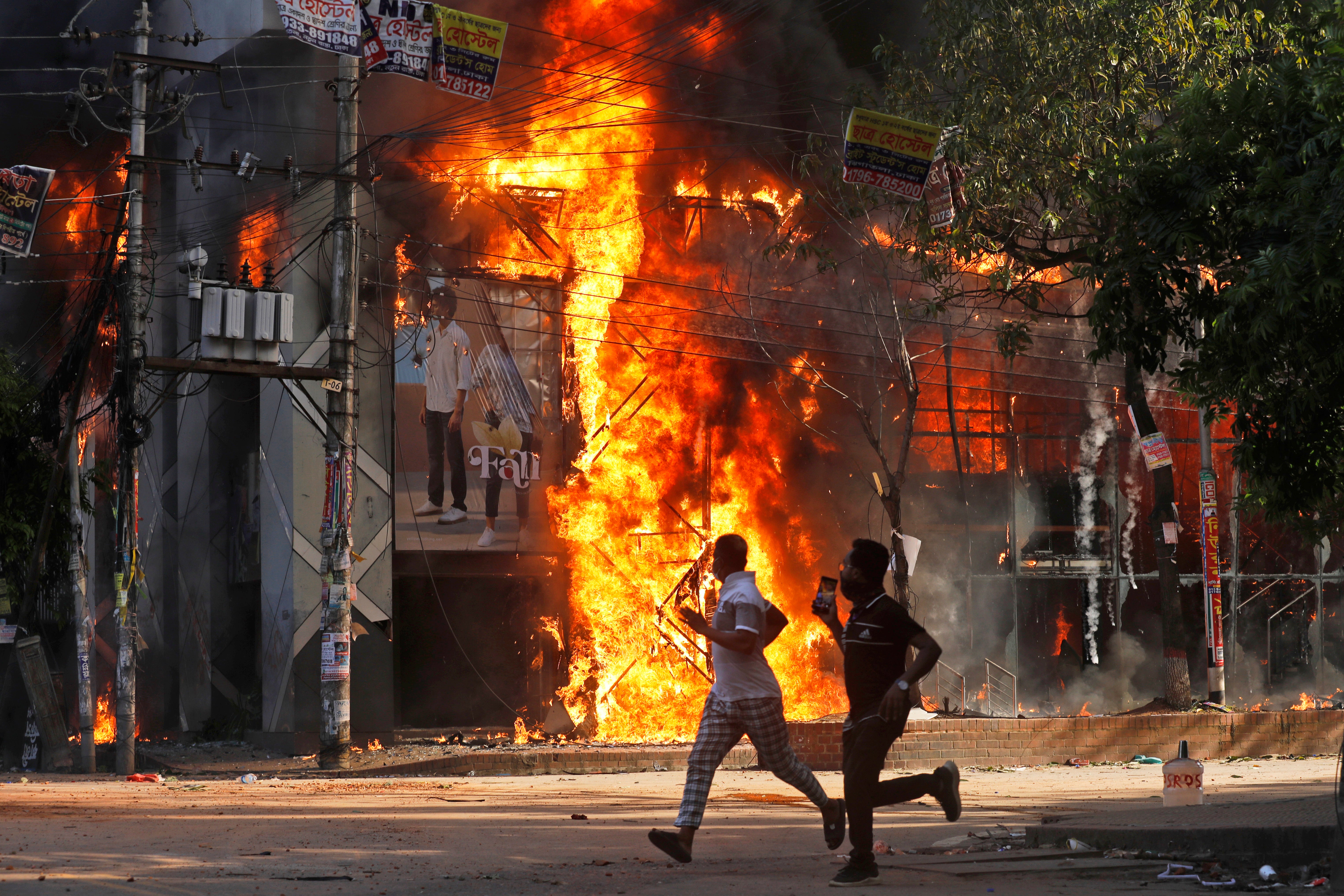 Men run past a shopping center which was set on fire by protesters during a rally against Sheikh Hasina