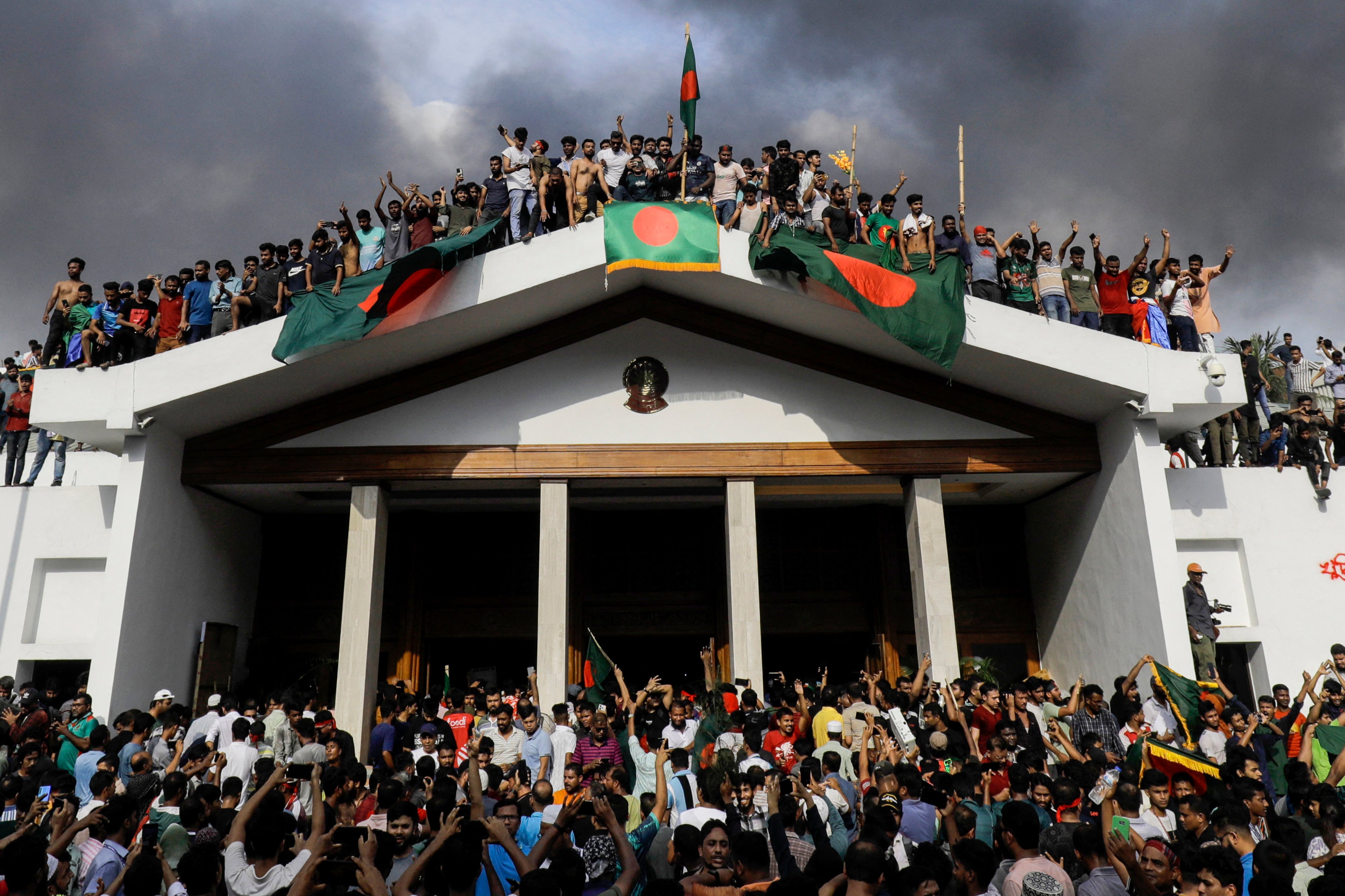 Protestors display Bangladesh's national flag as they storm prime minister Sheikh Hasina's residence in Dhaka on 5 August