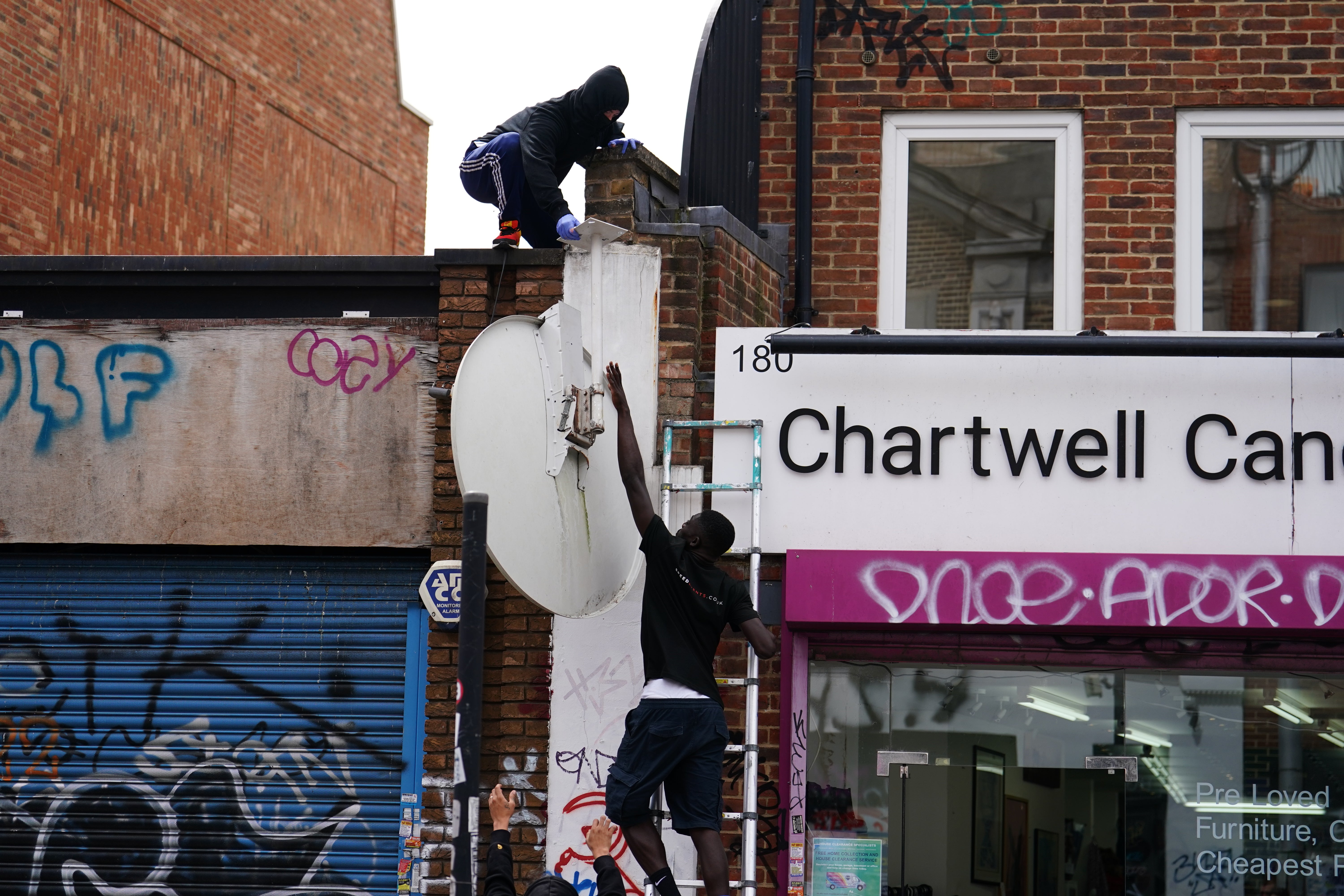 People remove a new artwork by Banksy from the roof of a shop in Peckham