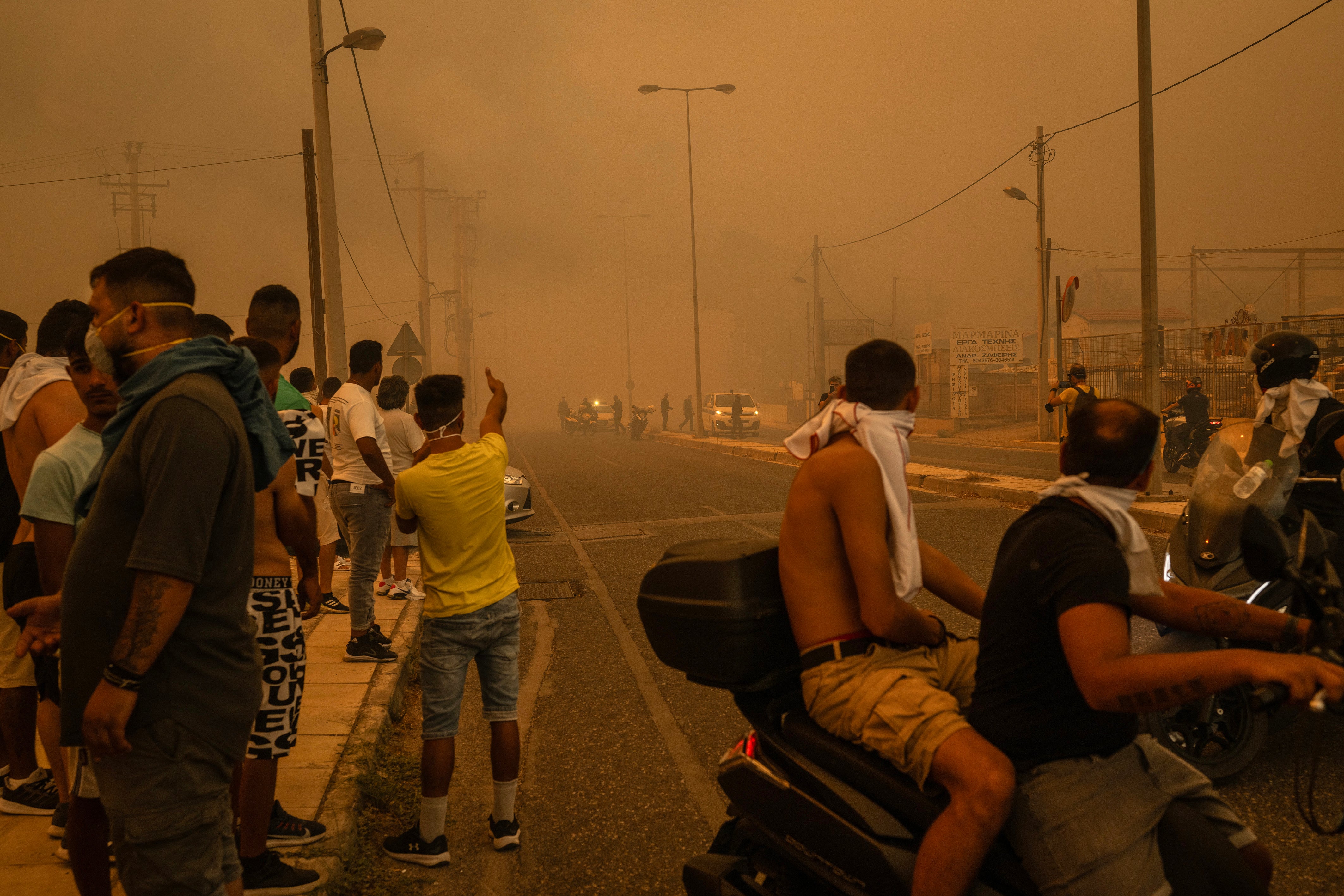 Local residents protect their mouths from the thick smoke caused by a wildfire near Penteli