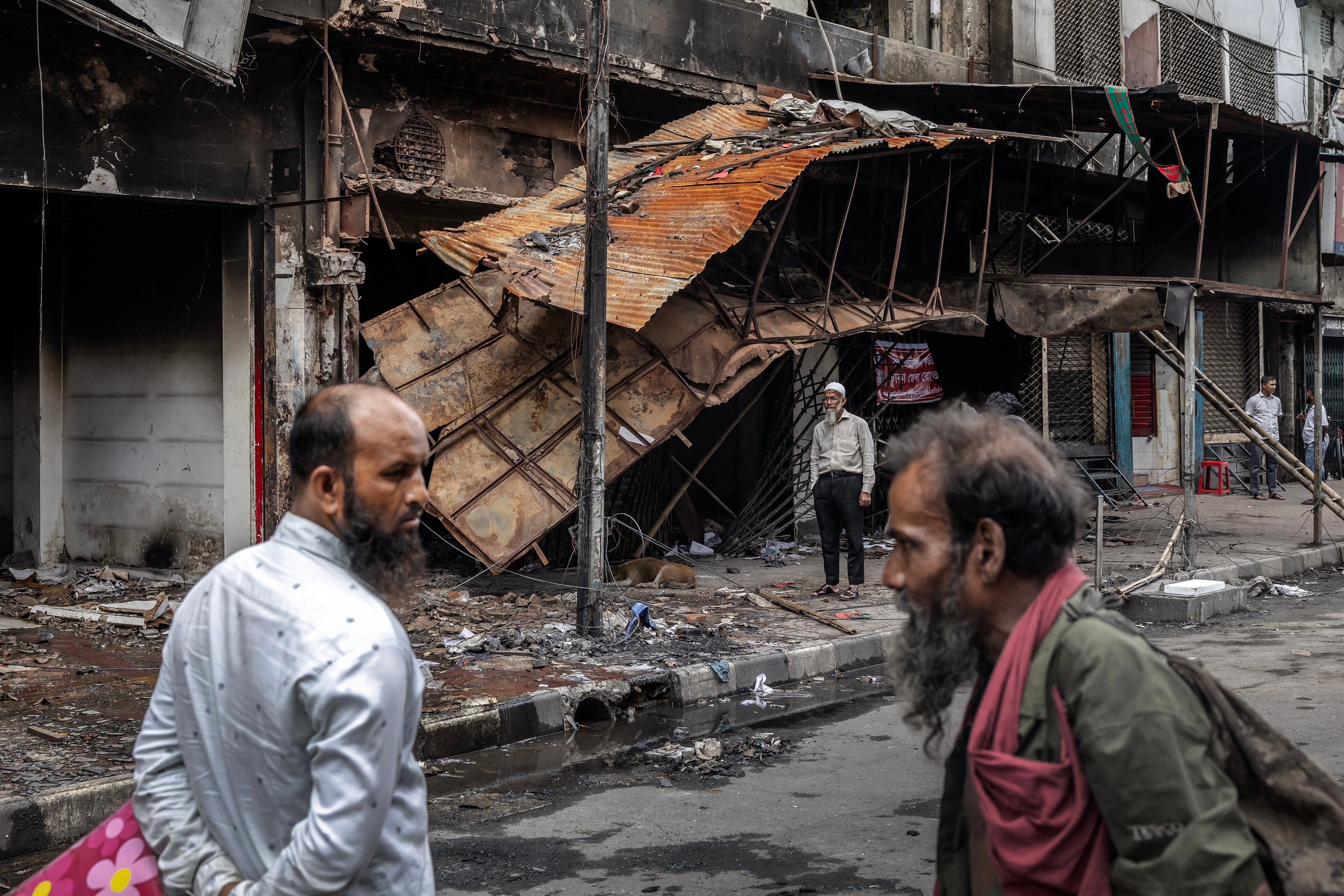 People walk past an office of the Awami League party and adjacent buildings that were vandalised and set on fire during the protests