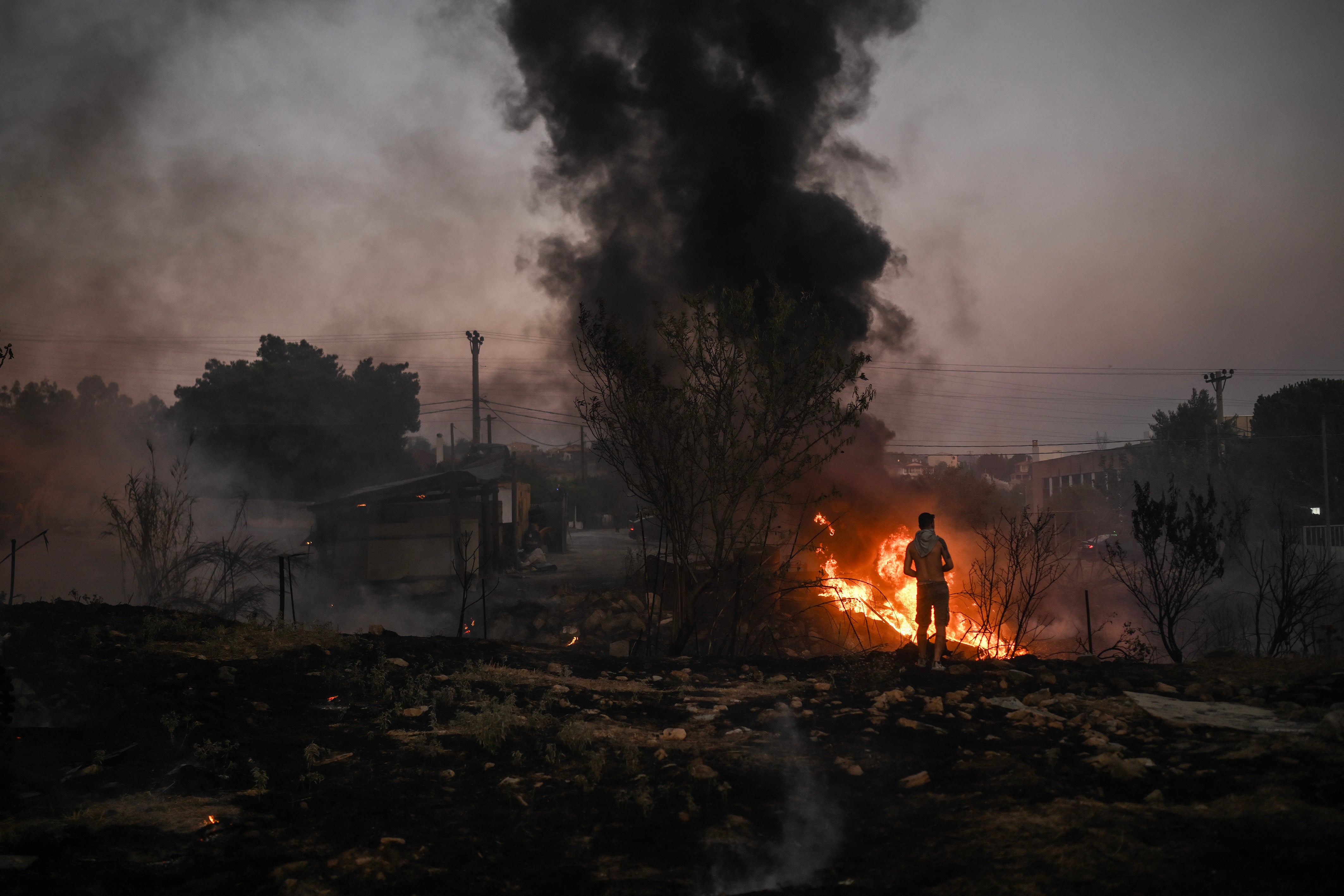 A volunteer stands in front of a small pocket of fire as wildfires burn near Penteli