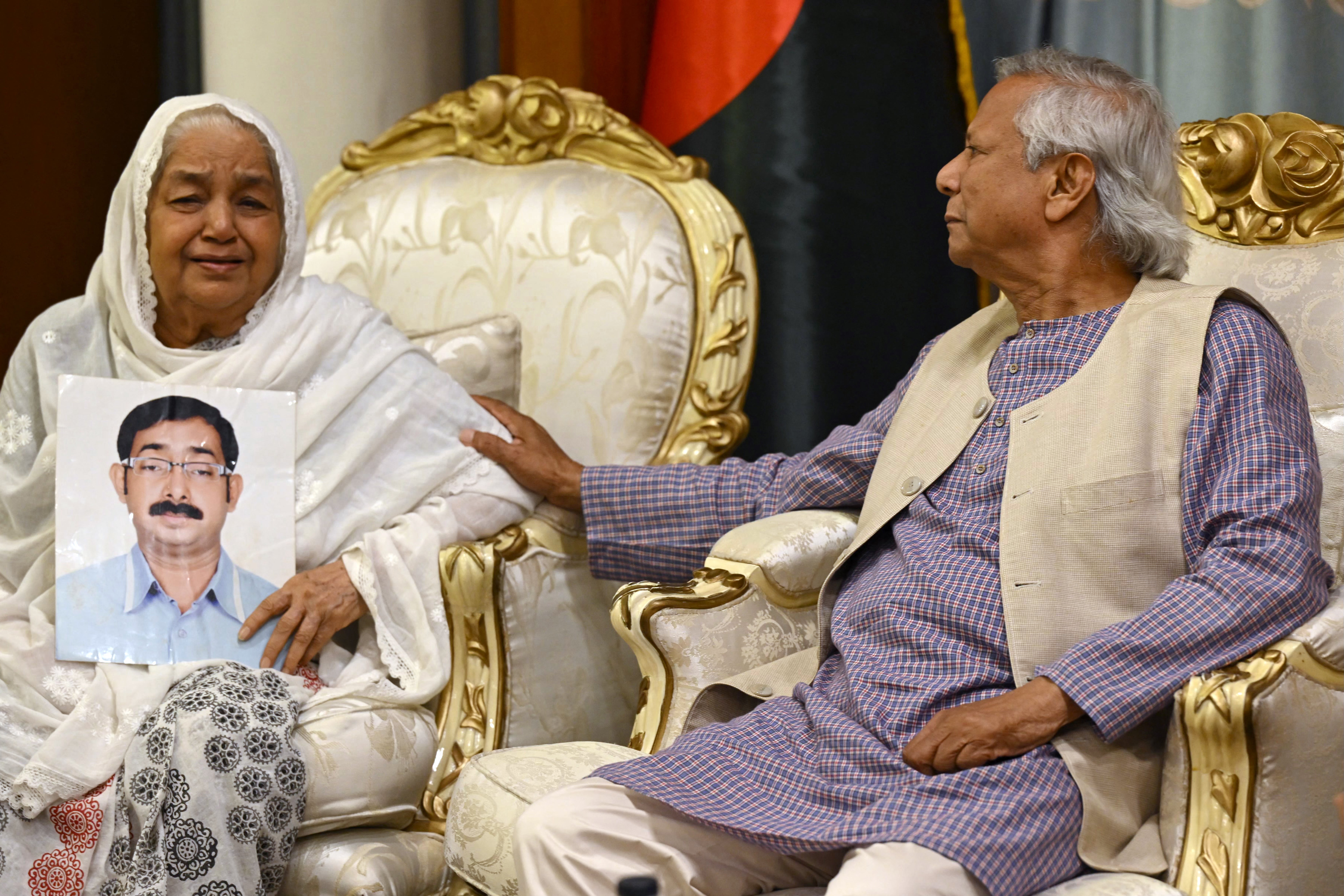 Bangladesh’s interim government Muhammad Yunus consoles Hazera Khatun as she holds a portrait of her son Sajedul Islam Sumon, who went missing during the rule of Sheikh Hasina, in Dhaka