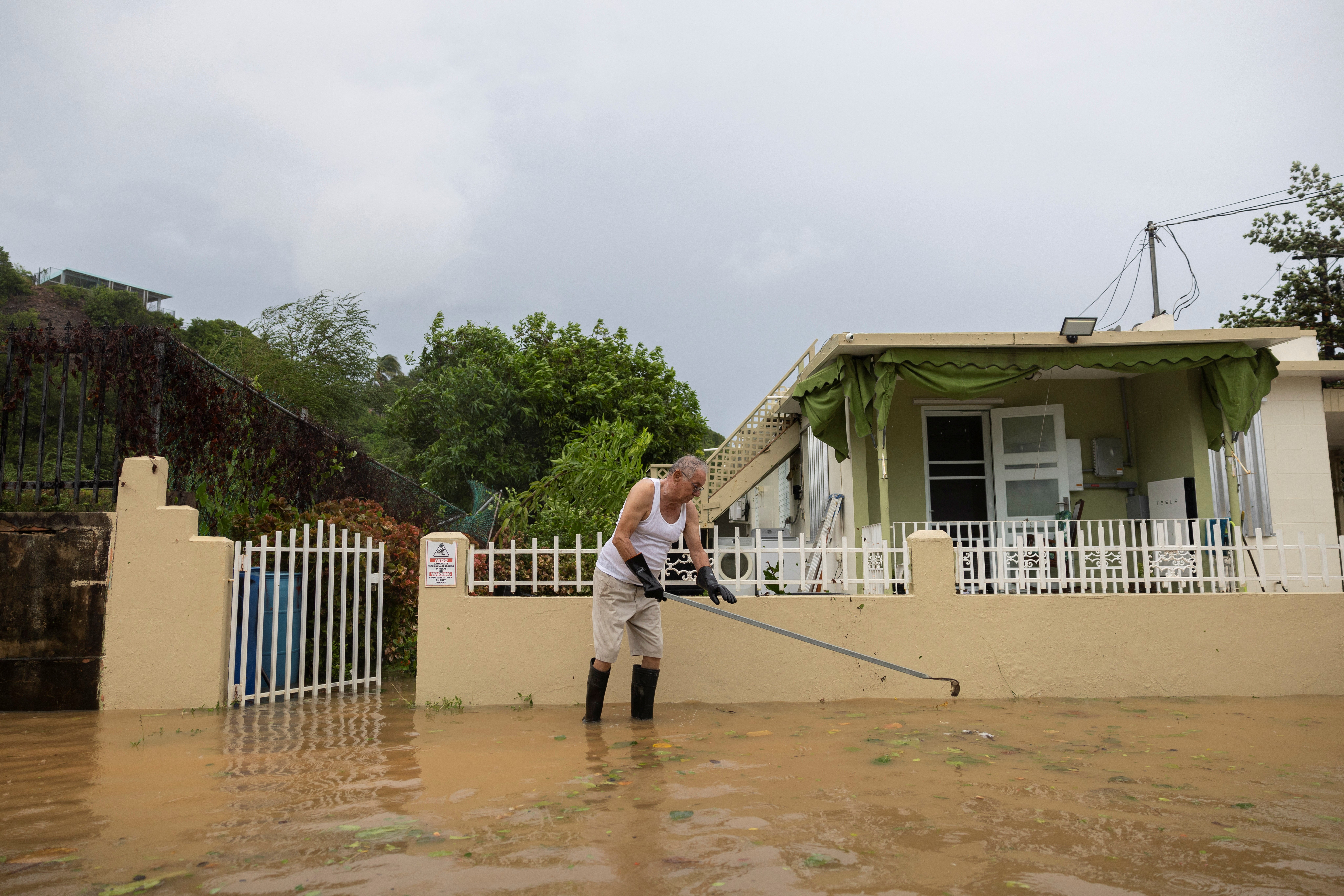 A man stands in floodwaters while unclogging a drain in Fajardo, Puerto Rico on Wednesday. Nearly 300,000 residents are still without power